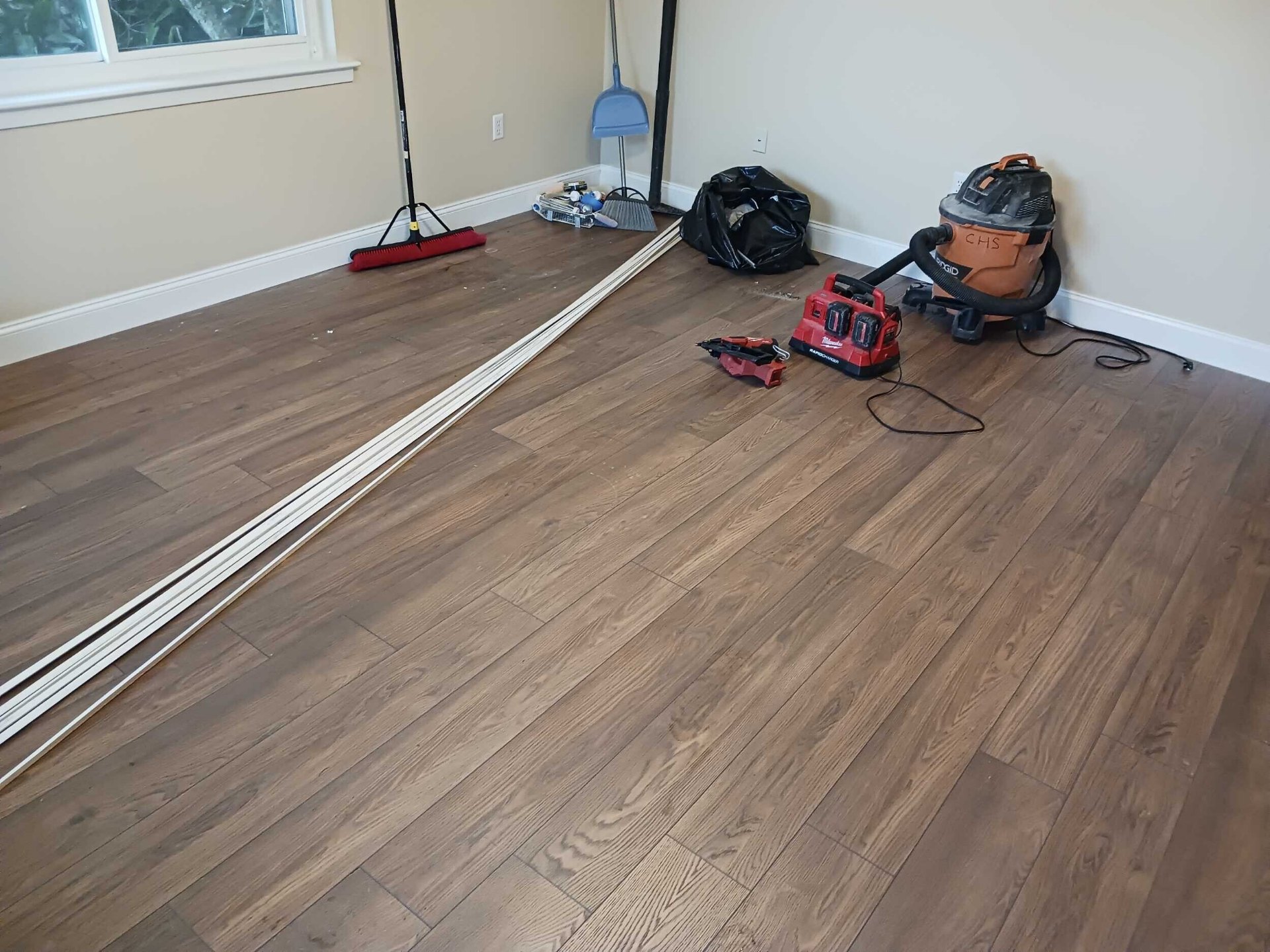 Finished new laminate flooring in the rebuilt Gretna living room with Cajun Home Services shop vac and tools staged for final cleanup