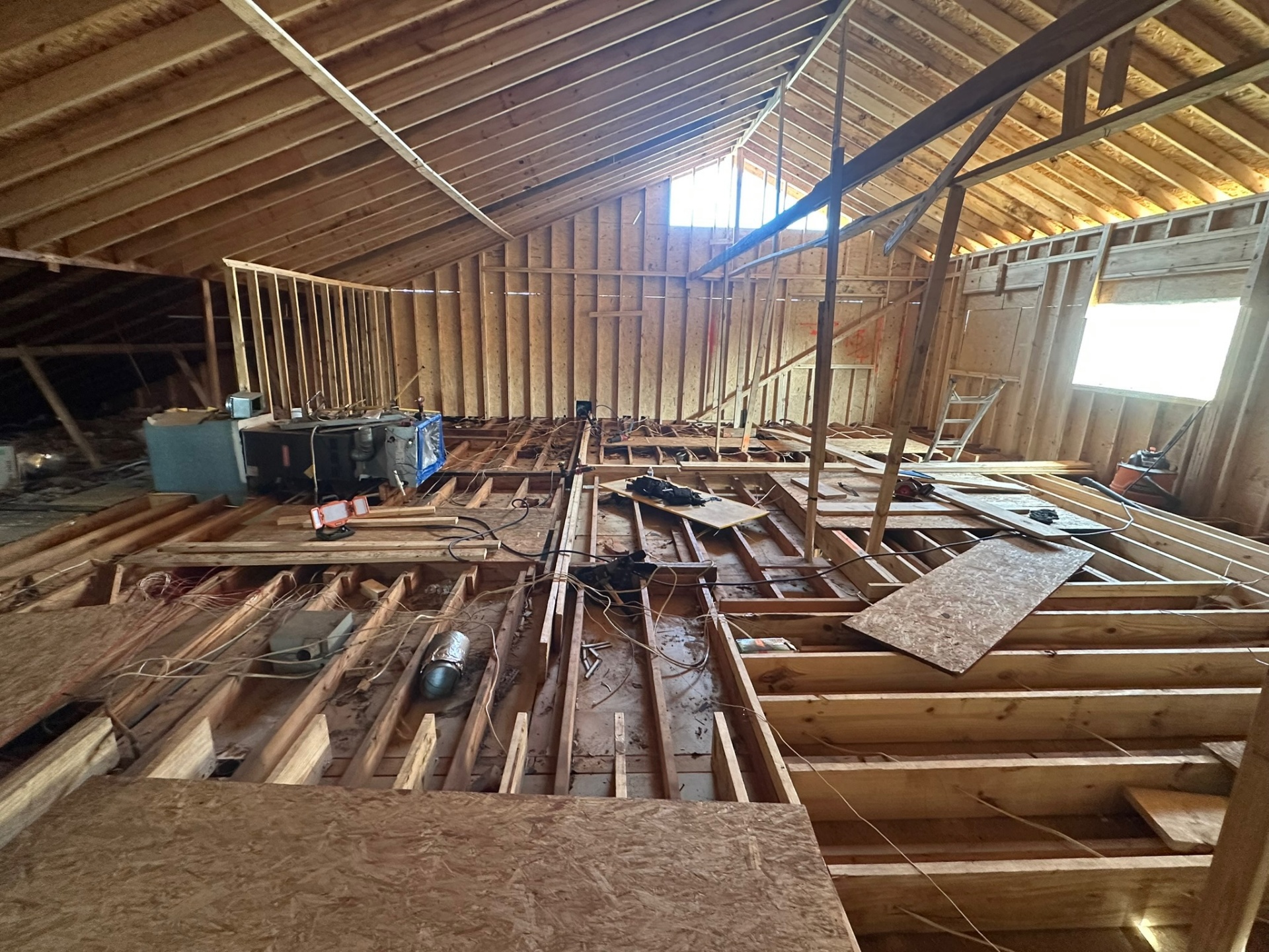 Wide interior view inside Metairie attic with original ceiling joists exposed, new wall framing started and HVAC equipment visible during second-floor addition prep