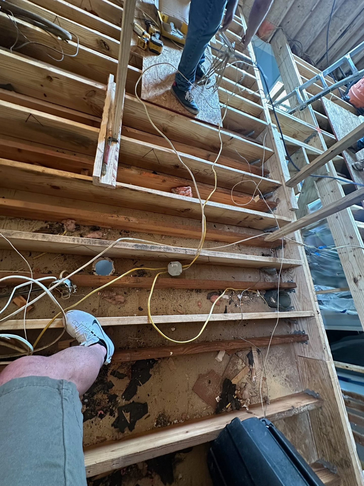 First-person view standing on existing ceiling joists inside Metairie attic with old wiring being pulled and decking partially removed before second-floor framing