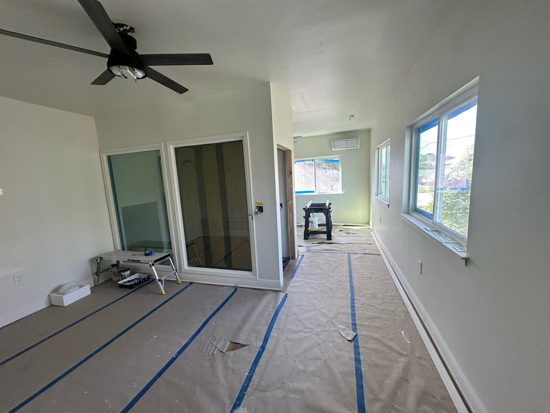 Loft area in Metairie second-floor addition with two interior sliding glass doors to master suite, large ceiling fan, banks of windows and floor masked for paint