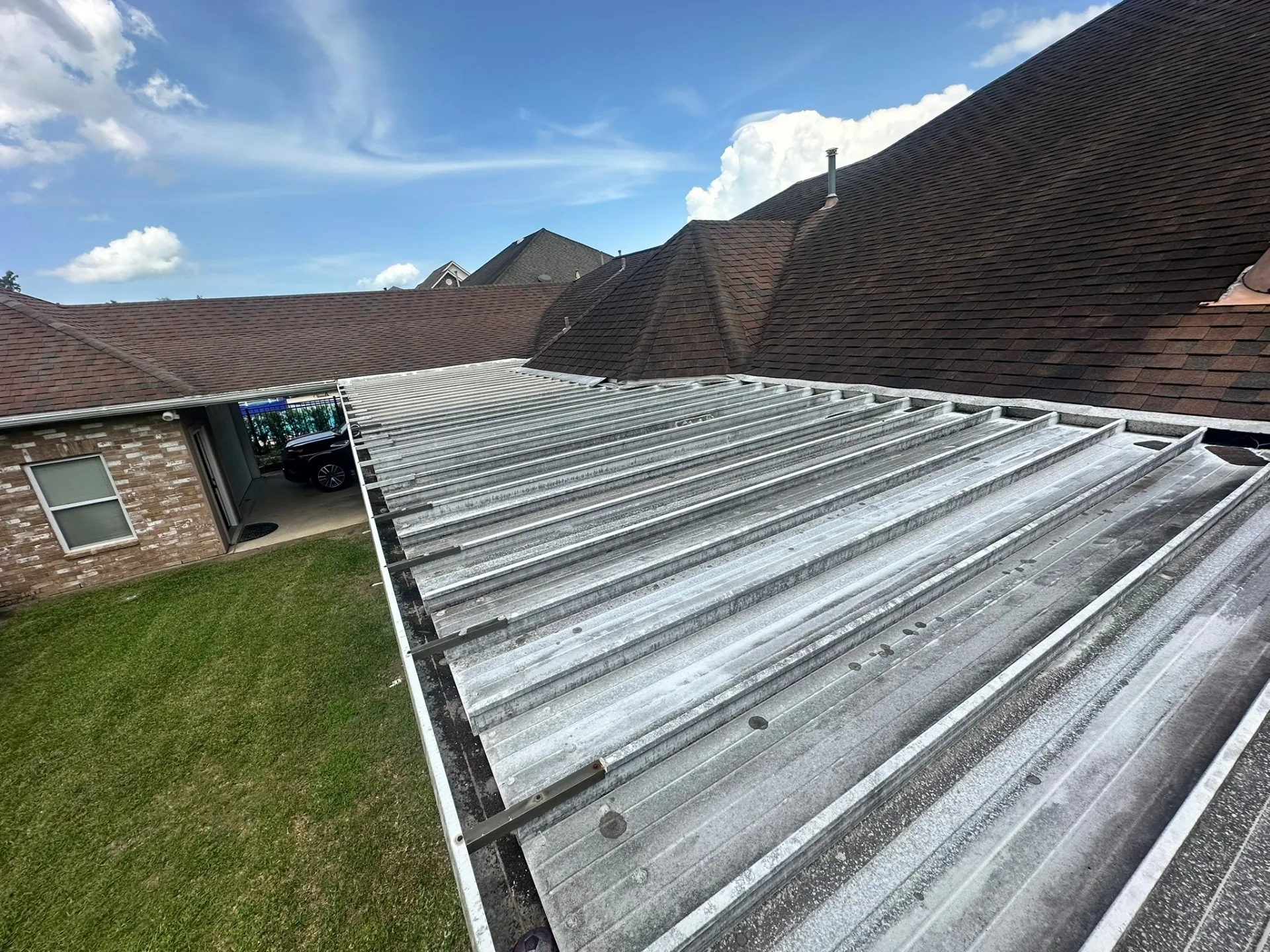 Aerial view of aged corrugated aluminum pan patio roof tied against main shingle roof of Destrehan Louisiana home before Cajun Home Services complete patio replacement