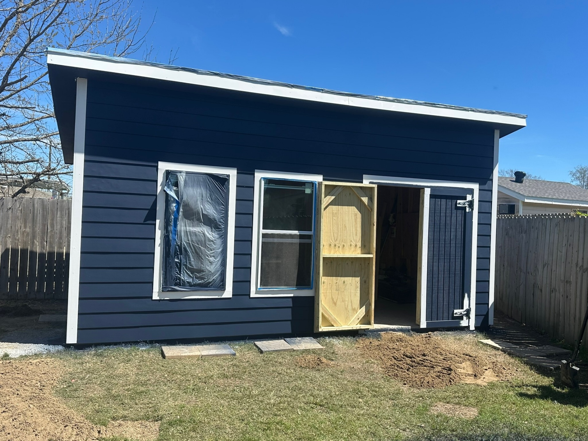 Front elevation of Metairie shed showing painted Hardie siding, white window trim, and new pressure-treated door before stain
