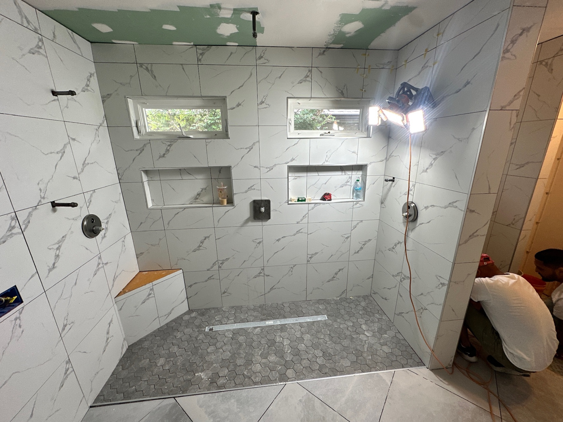 Walk-in shower fully tiled with dual valves, dual niches, bench, and hex floor before grout in Metairie master bath