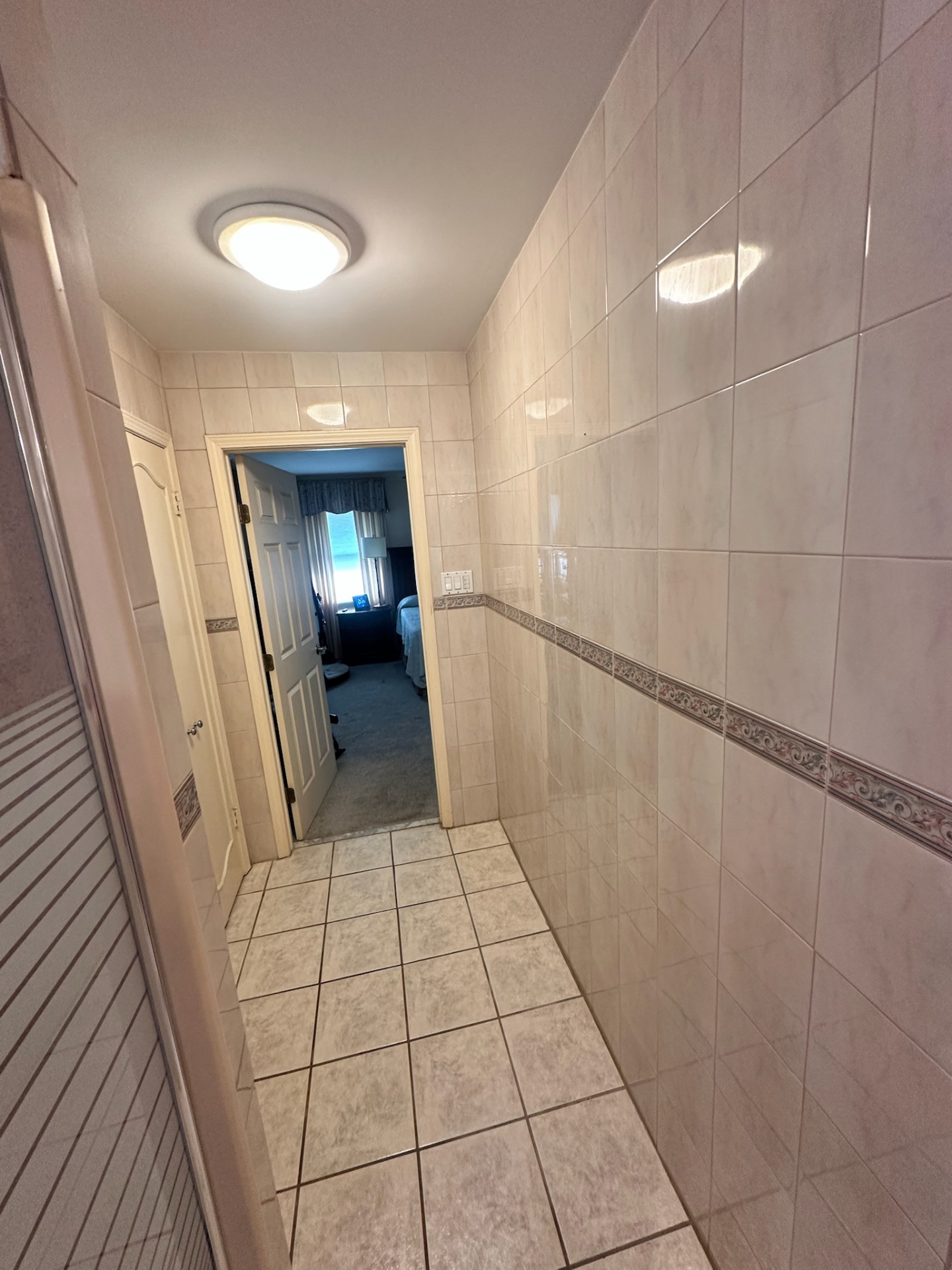 Before — narrow tiled hallway entry to Metairie master bathroom with floral border tile