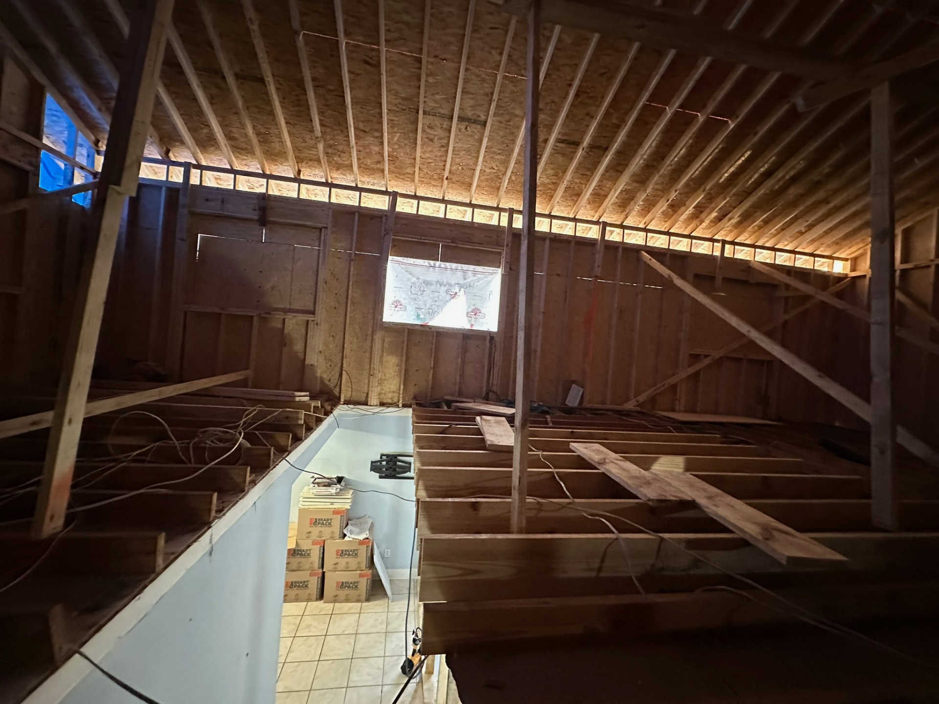 Wide interior view of new second-floor joists and partial wall framing with Tyvek-wrapped gable opening on Metairie addition