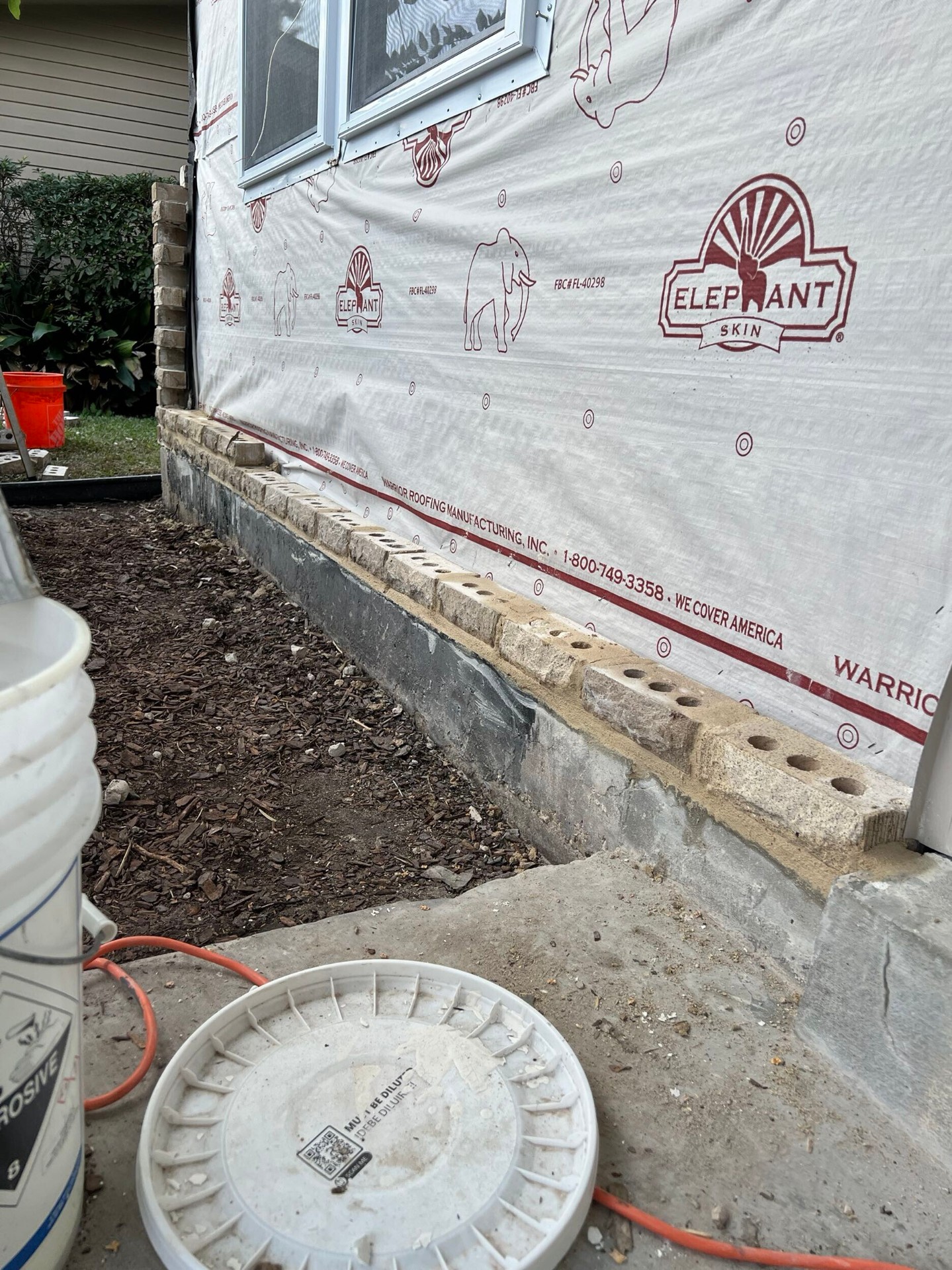 First courses of new brick veneer laid on the rebuilt Gretna wall against the house wrap, tying into the original foundation