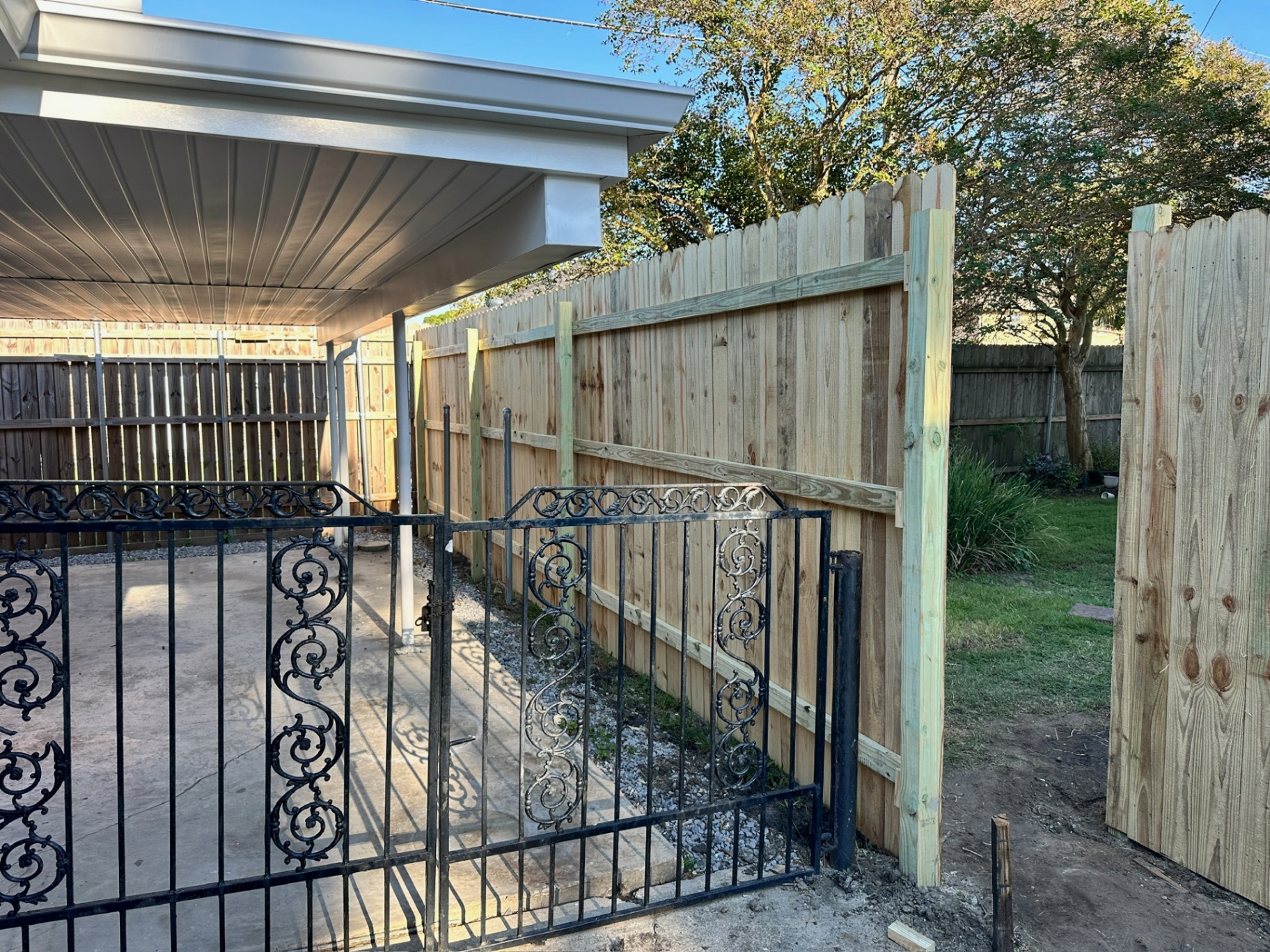 New treated picket privacy fence tied into the existing carport and wrought iron driveway gate at the Bissonet Dr Metairie home
