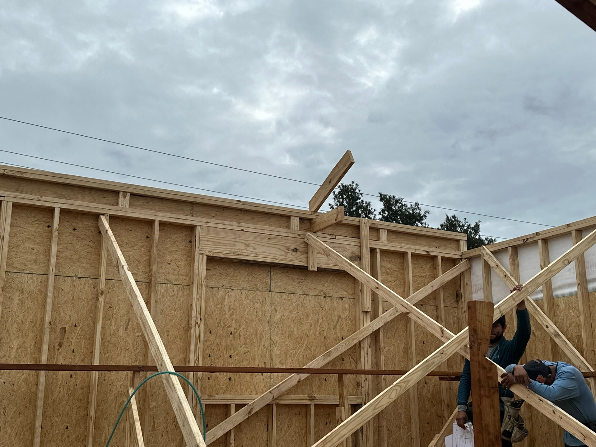 Carpenters installing new second-floor wall framing on Metairie addition with diagonal X-bracing holding sheathed walls plumb against cloudy sky