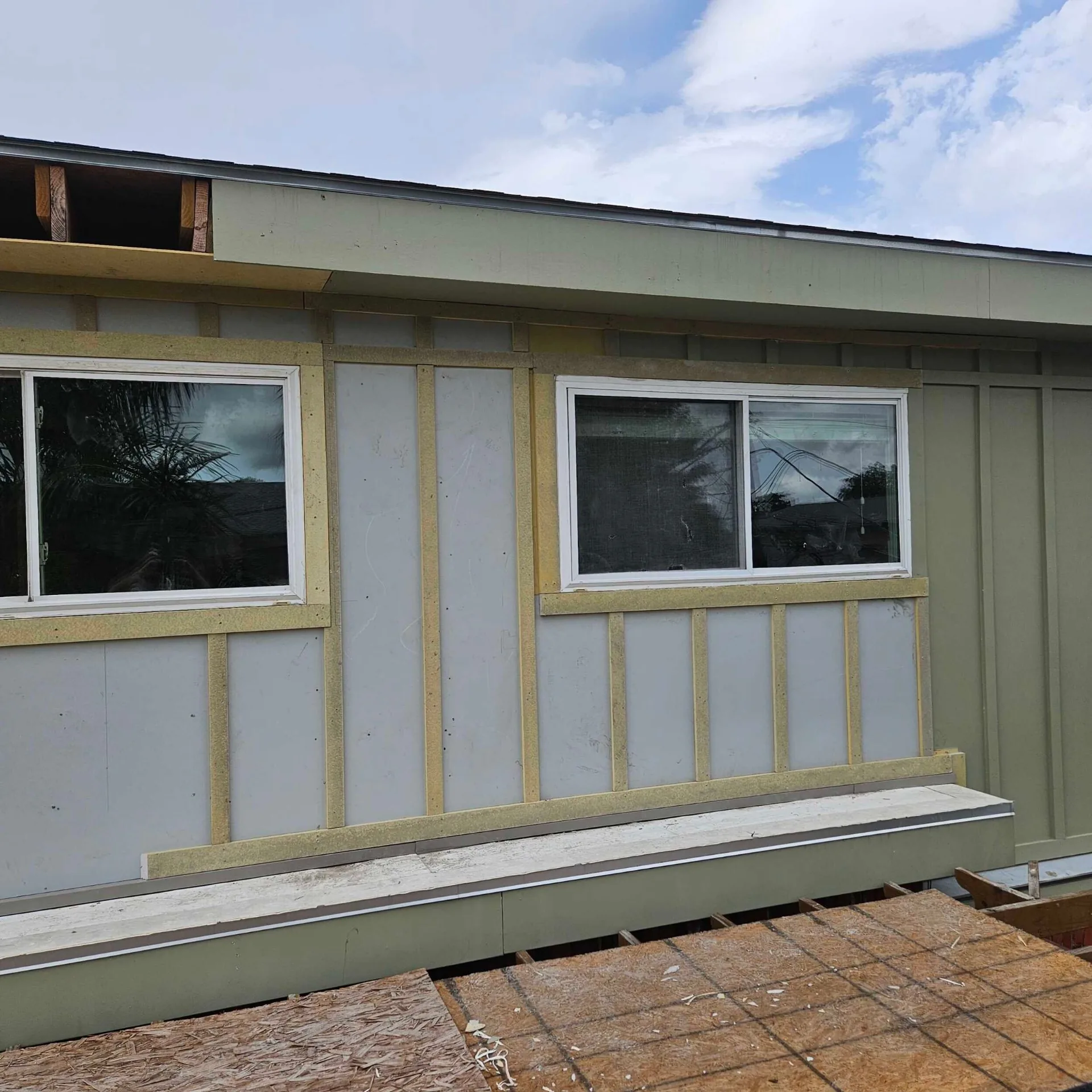 Rear elevation of Blanke Street Metairie home with new board-and-batten siding in primer, yellow battens over gray field, second-story addition wall framed and sheathed