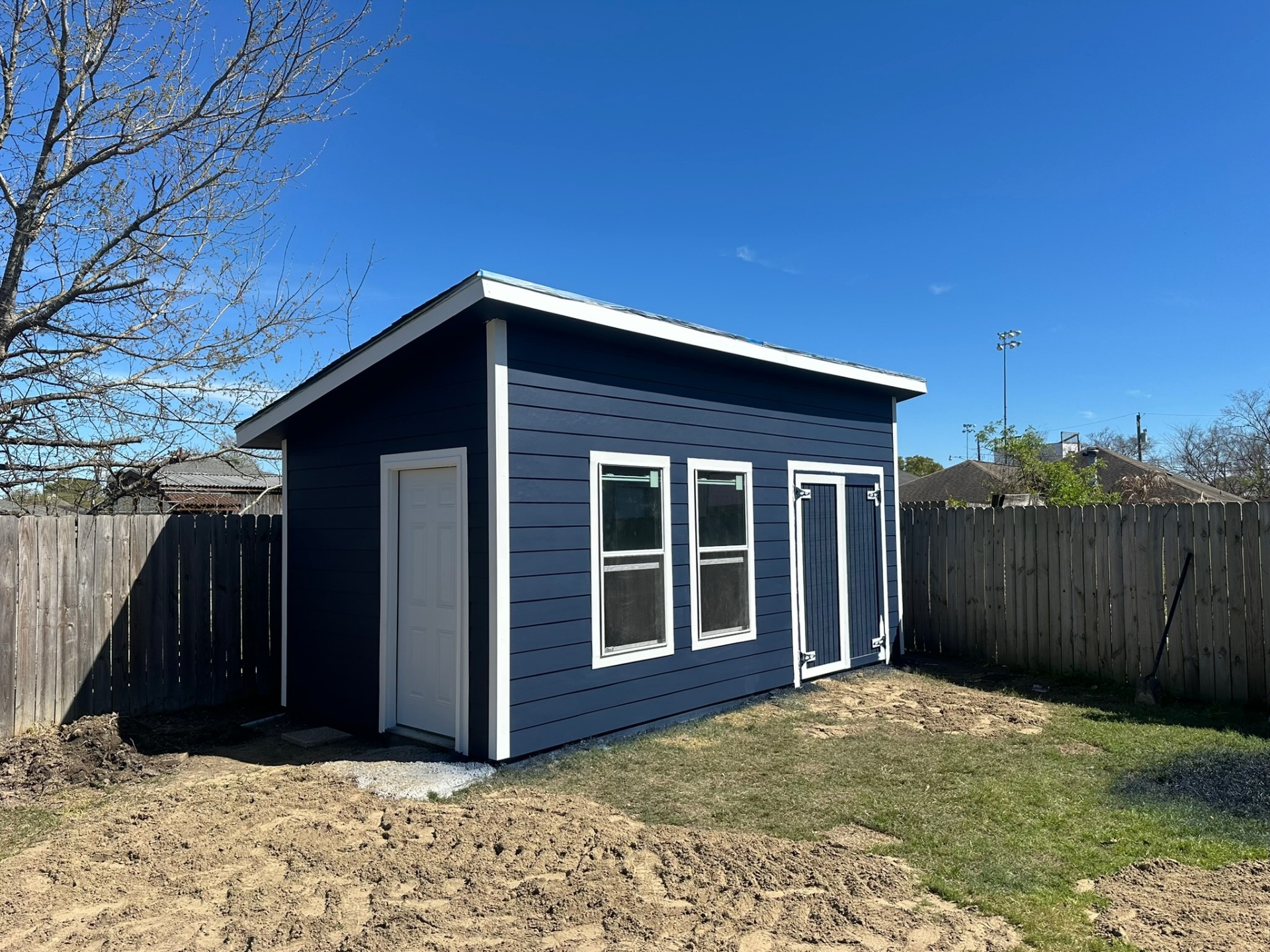 Completed Metairie outbuilding from three-quarter angle showing navy Hardie siding, white trim, double barn doors, side entry door, and dual windows