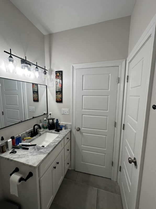 Finished bathroom vanity area in Meraux LA remodel with marble top, undermount sink, matte black hardware, and large black framed vanity mirror under a black four-globe vanity light