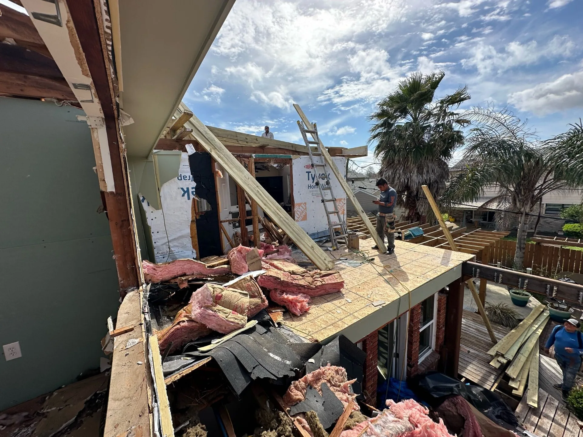 Rear elevation of Blanke Street Metairie home mid-demo with new plywood decking, Tyvek house wrap, and crew working the addition footprint