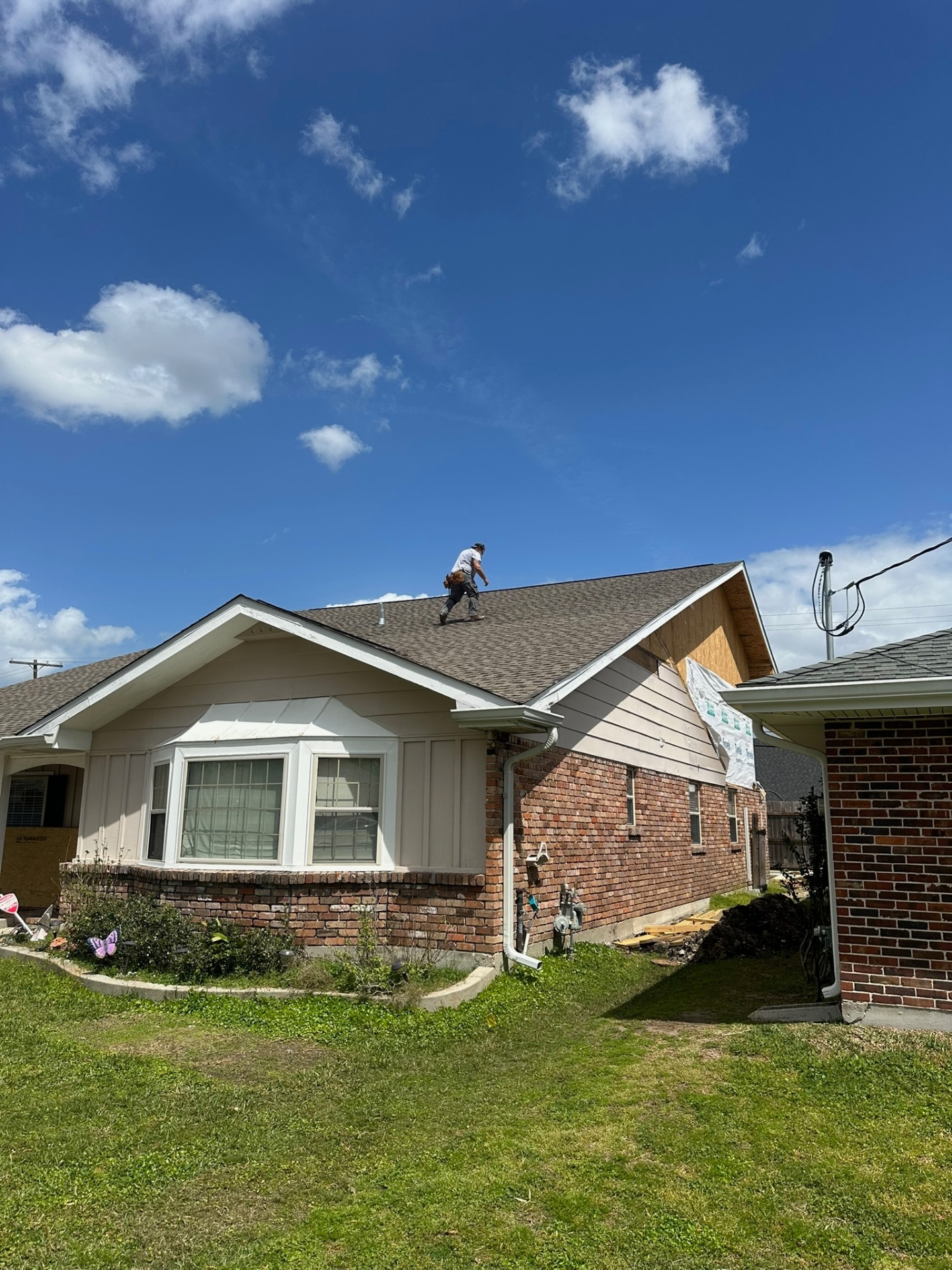 Roofer walking the ridge of the original single-story brick Metairie home inspecting the existing shingle roof and bay window before the second-floor addition tear-off begins