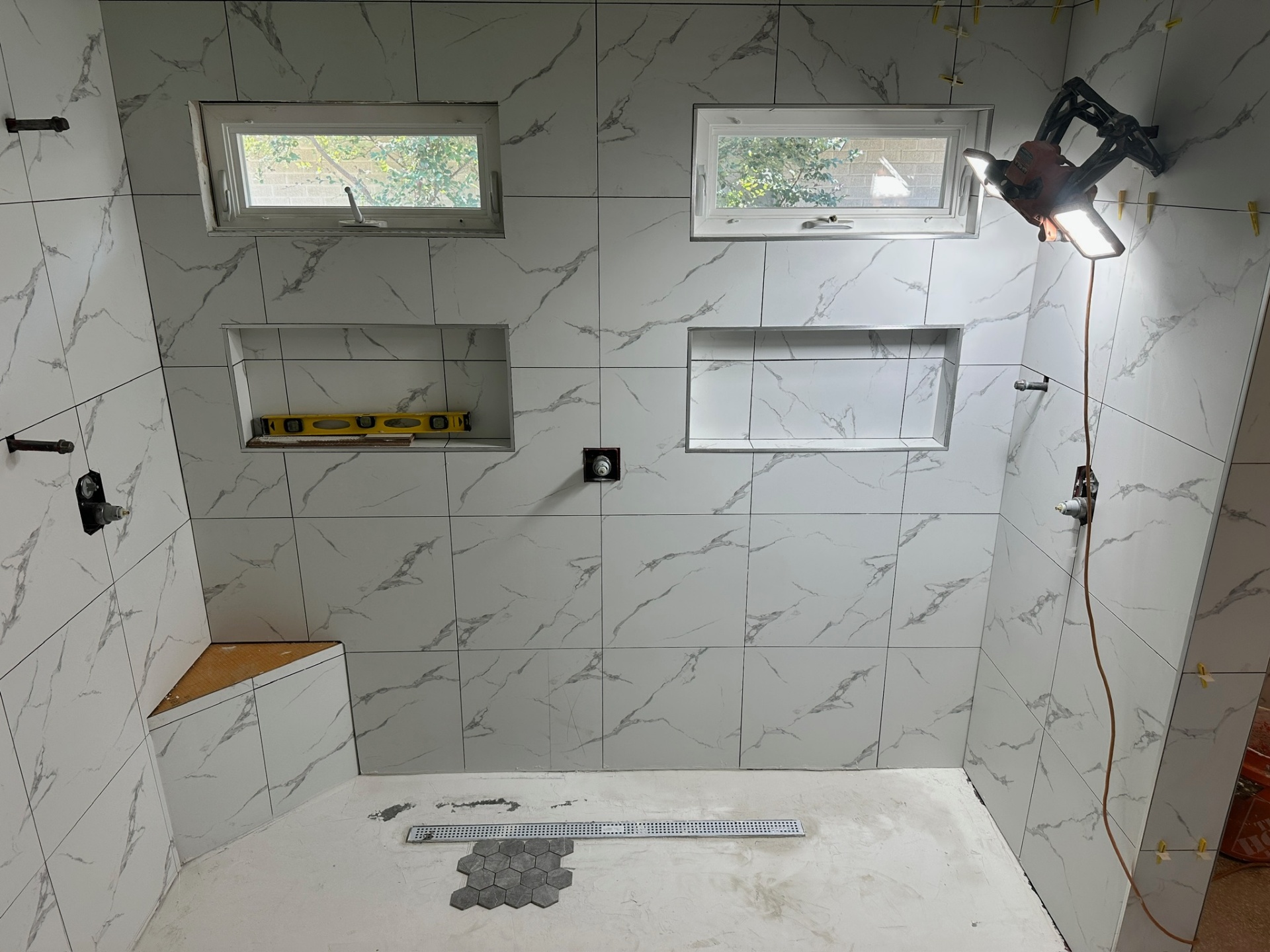 Walk-in shower with dual niches, dual awning windows, bench, and hex mosaic floor starting at the drain in Metairie master bath