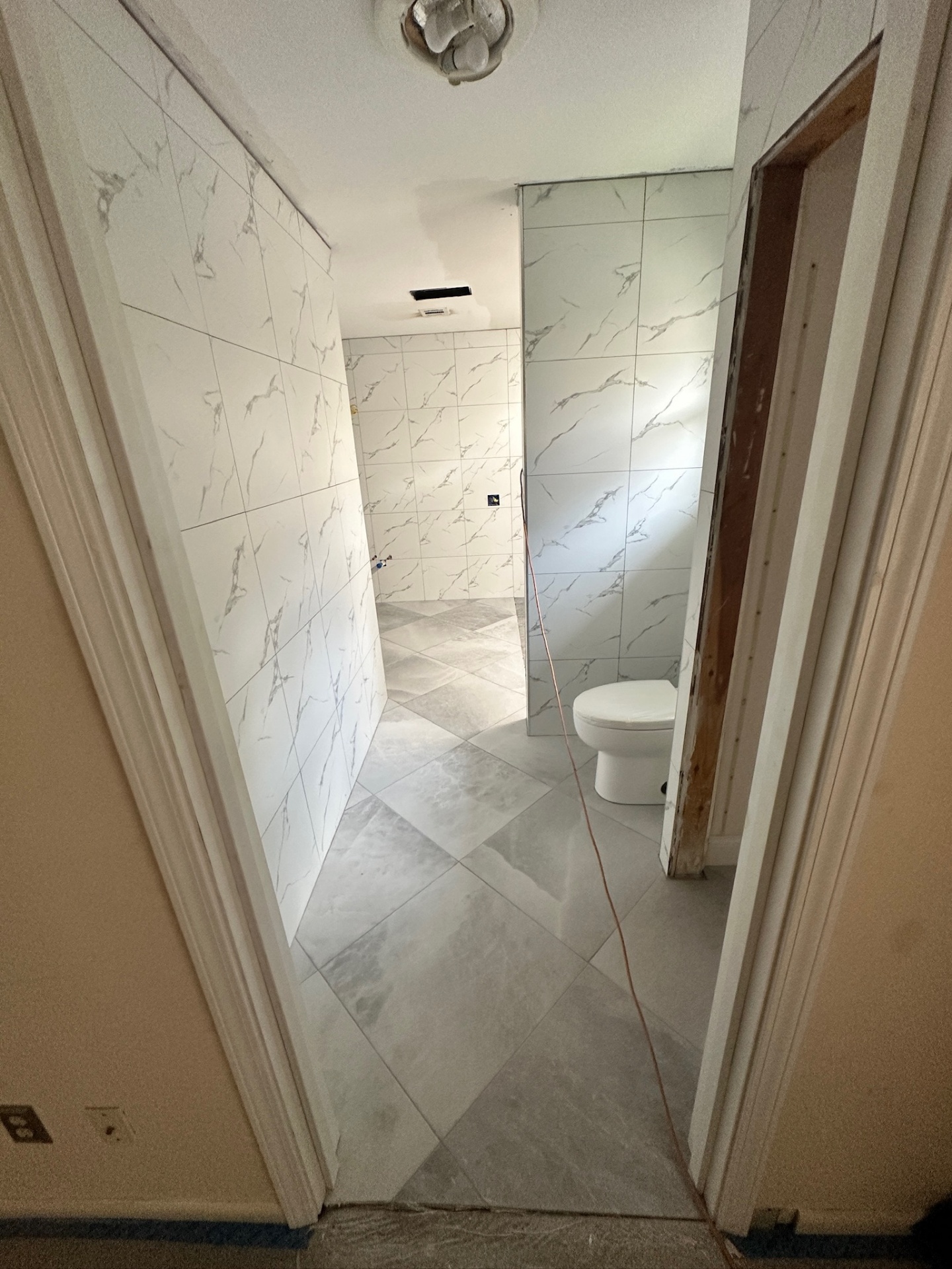 Finished tiled entry hallway with marble-look walls and floor looking into Metairie master bath