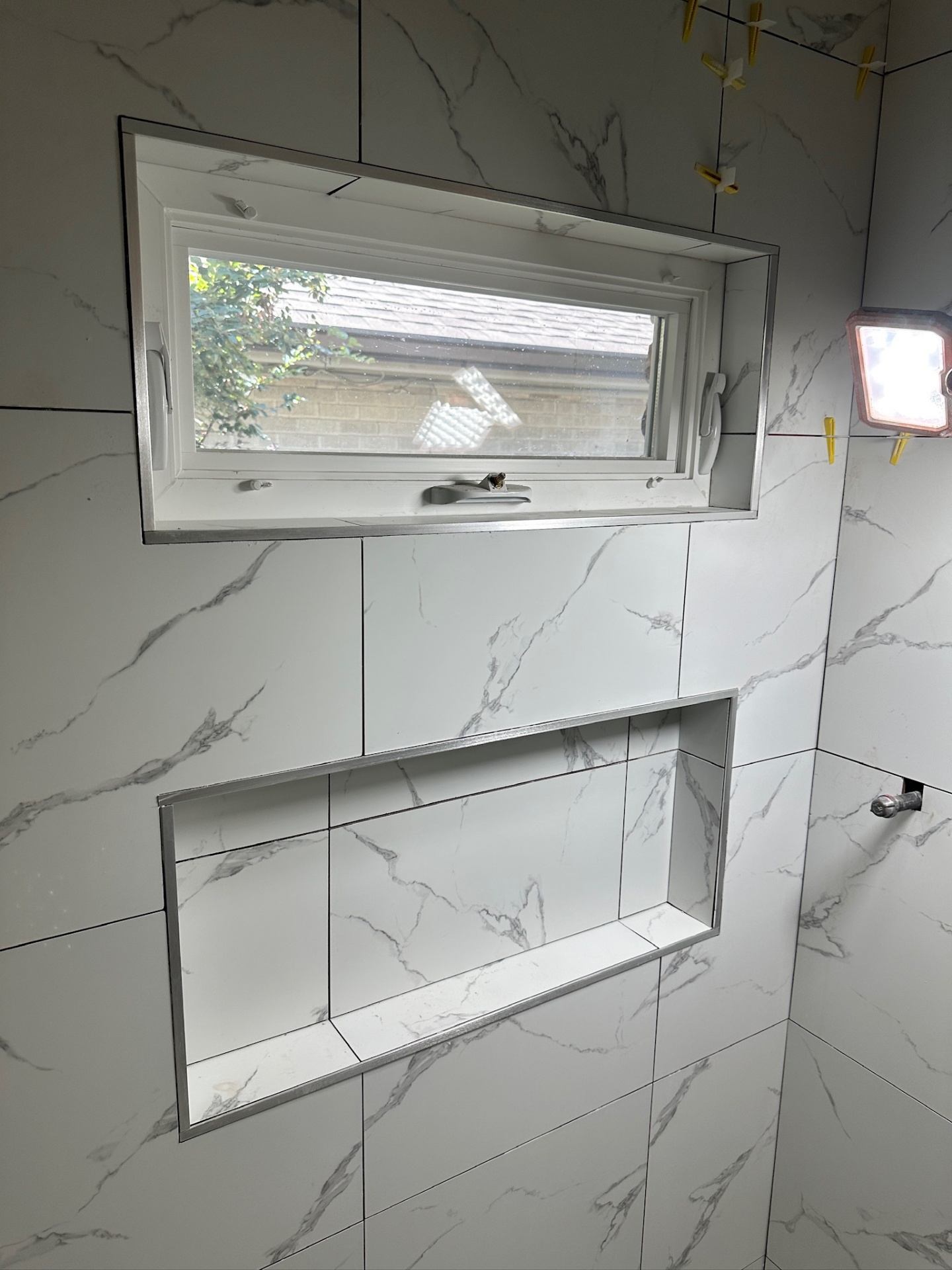 Finished shower niche and awning window with clean Schluter edges on marble-look porcelain in Metairie master bath