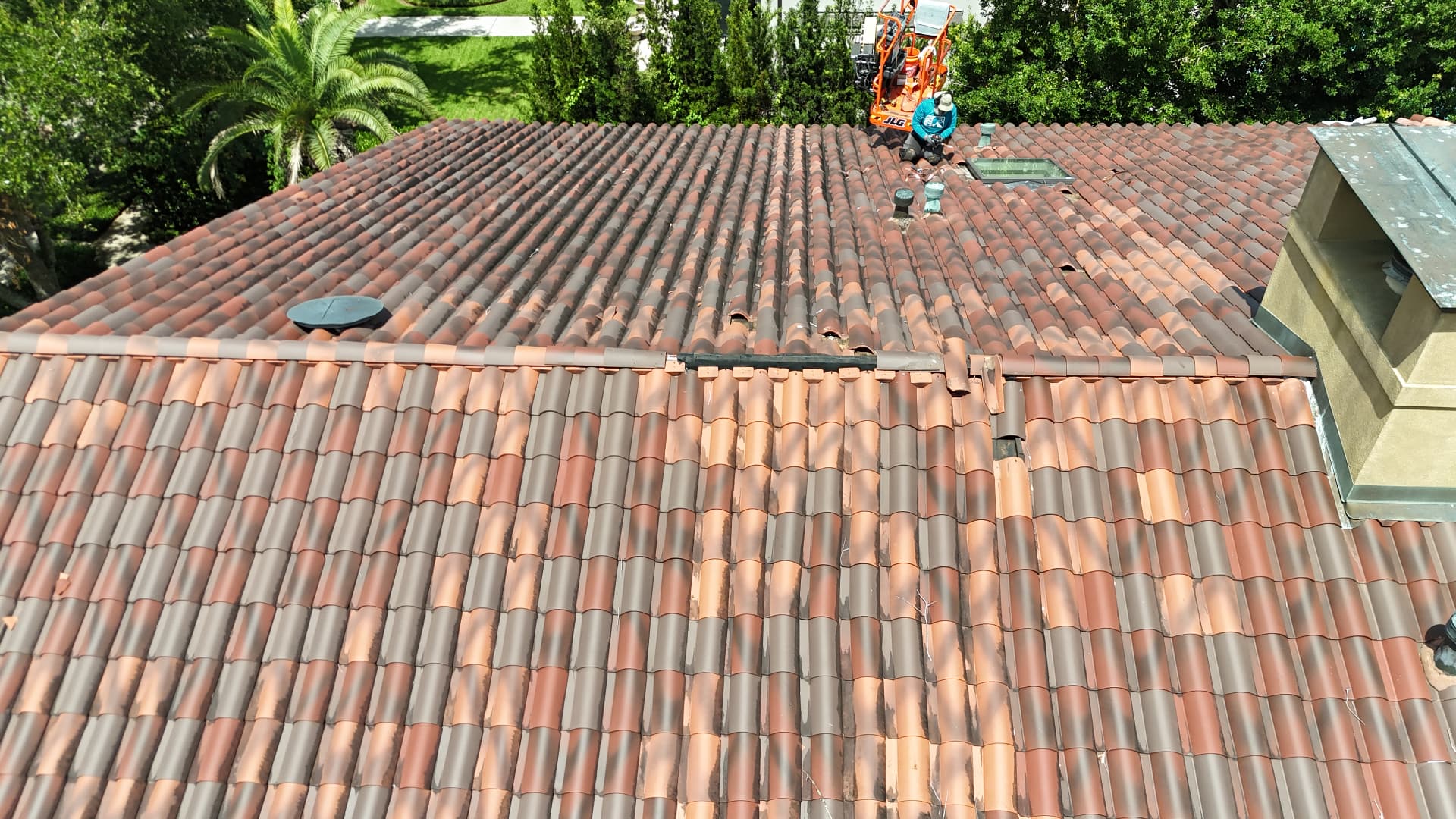 Aerial view of a Cajun Home Services roofer working from a boom lift on a large terra cotta tile roof in Metairie Louisiana