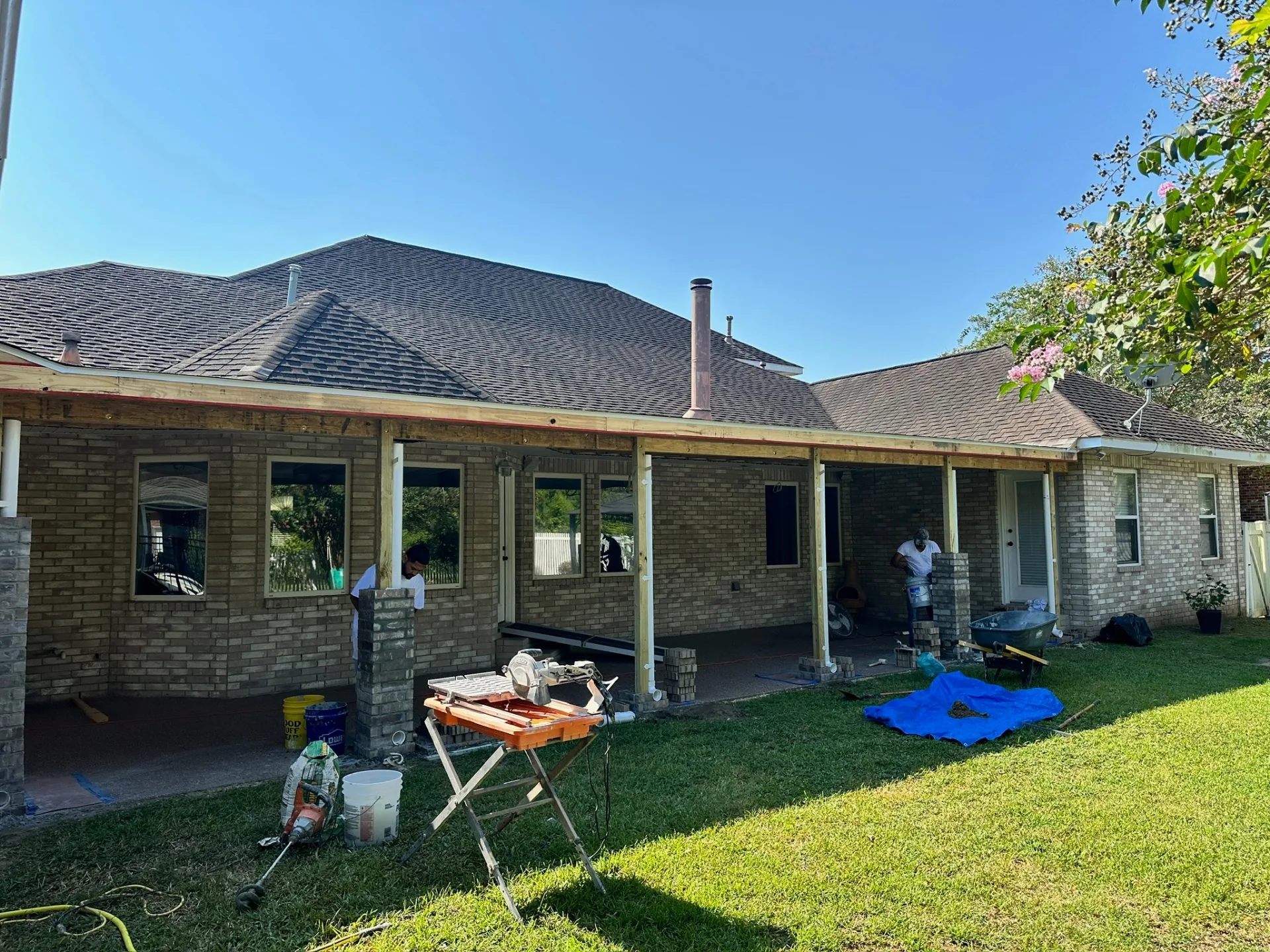 Rear elevation of Destrehan Louisiana home showing new shingle patio roof, framed overhang, and brick-wrapped posts being built by Cajun Home Services