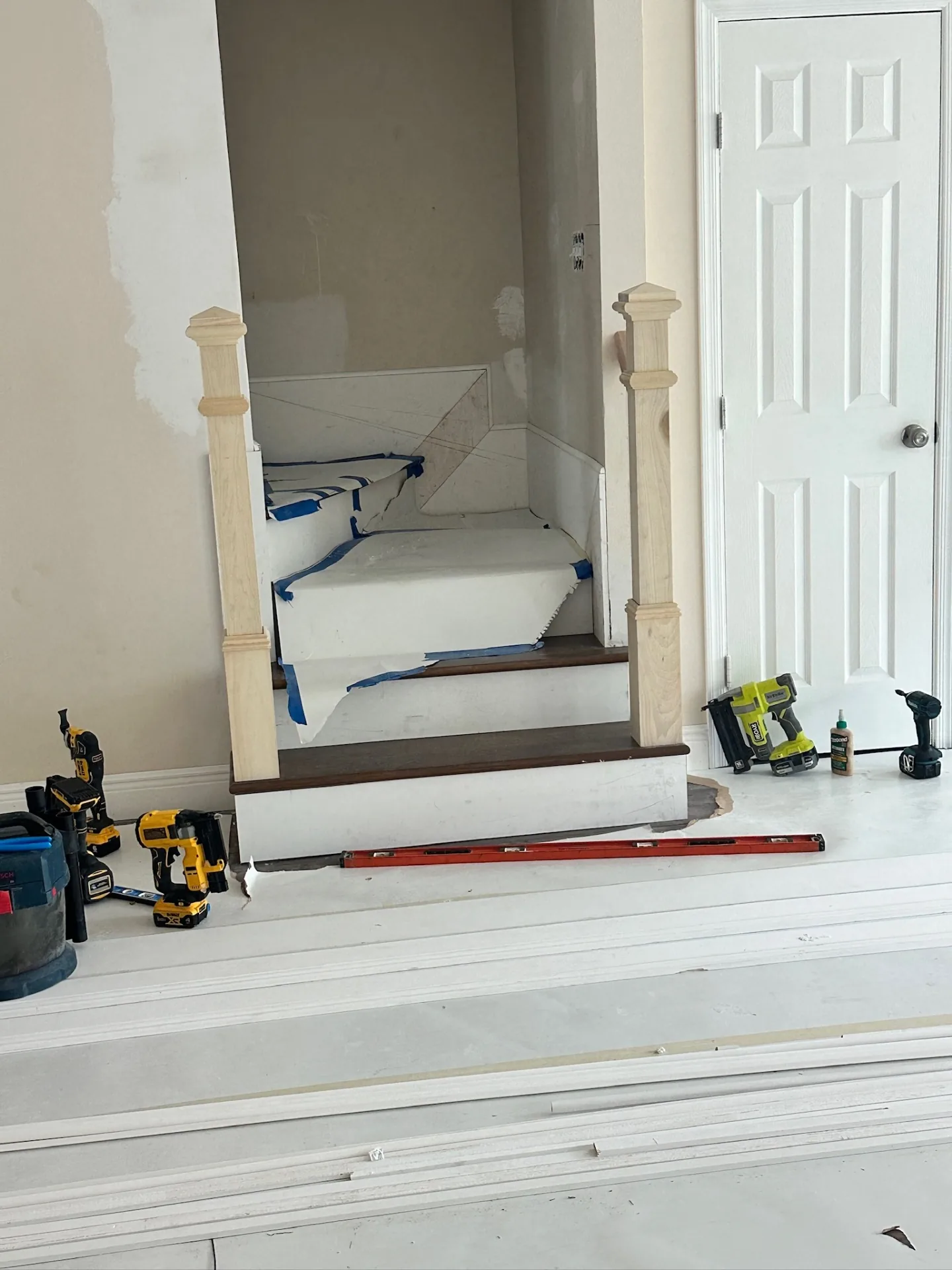 Turned wood newel posts primed and set at the base of the refinished stair at Blanke Street Metairie home, treads and risers papered off for finish work