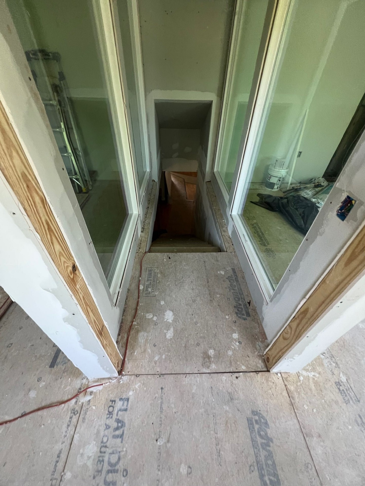 Second-floor stairwell opening on the Metairie addition framed with vertical wood posts and prepped with painted trim for an upcoming glass railing system, looking down into the stair landing