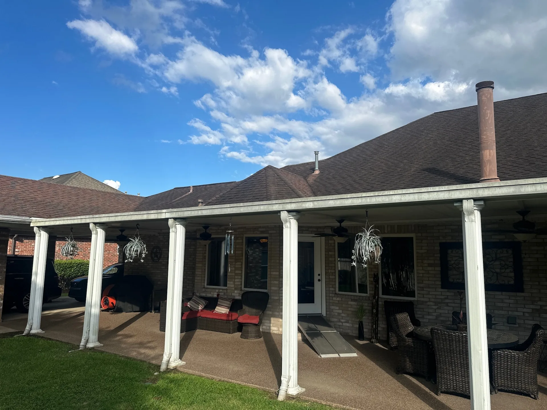 Rear elevation of Destrehan Louisiana brick home with existing weathered covered patio, shingle roof visible above, prior to Cajun Home Services complete patio replacement
