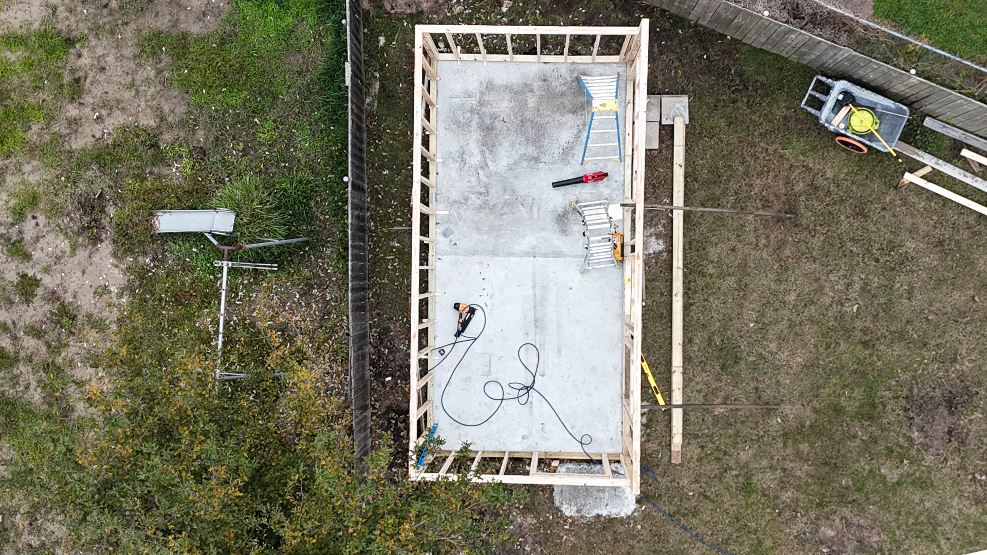 Aerial top-down drone view of fresh concrete slab with pressure-treated wall framing started for Metairie outbuilding