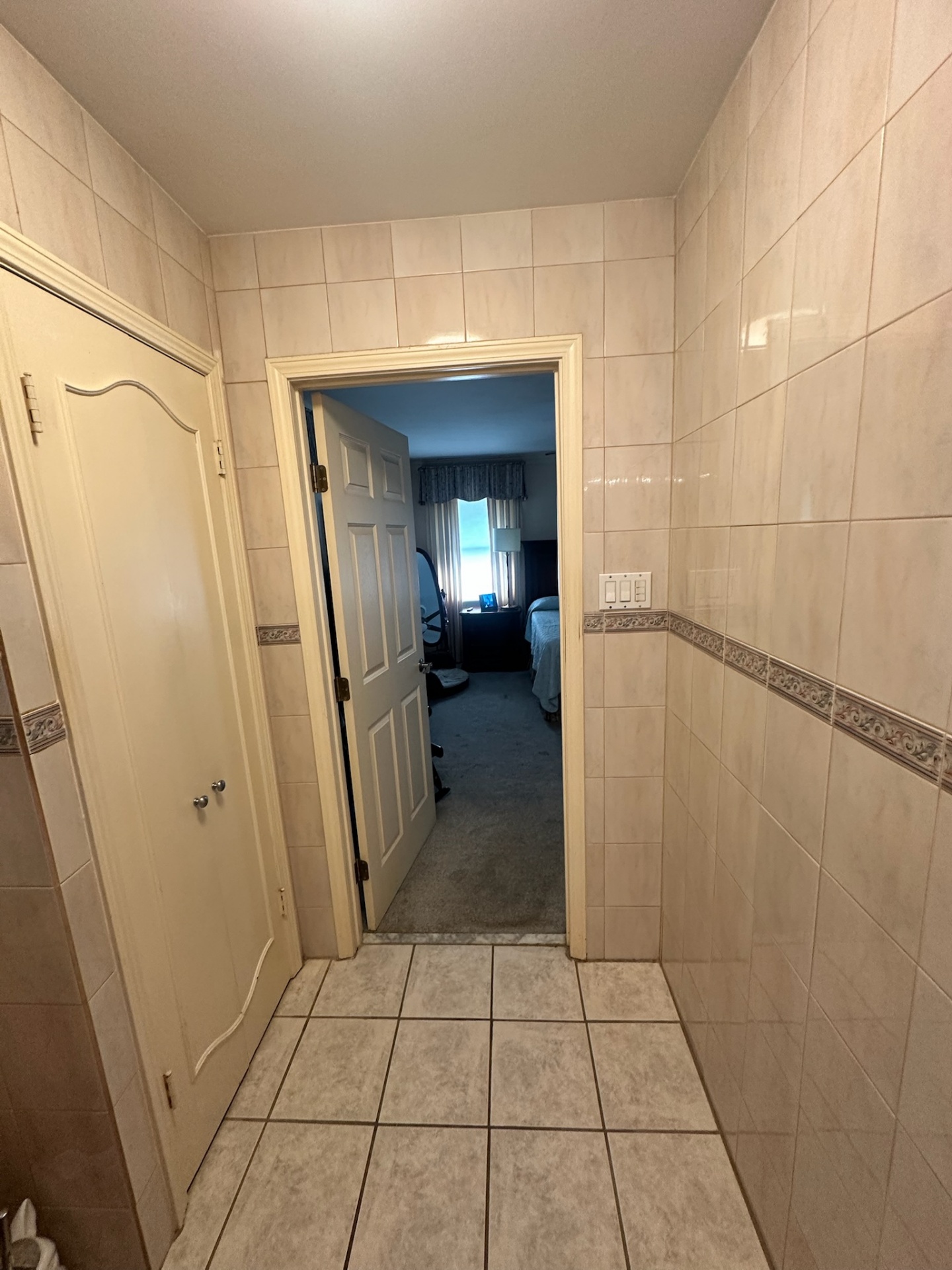 Before — narrow tiled entry hallway looking into the master bedroom in Metairie