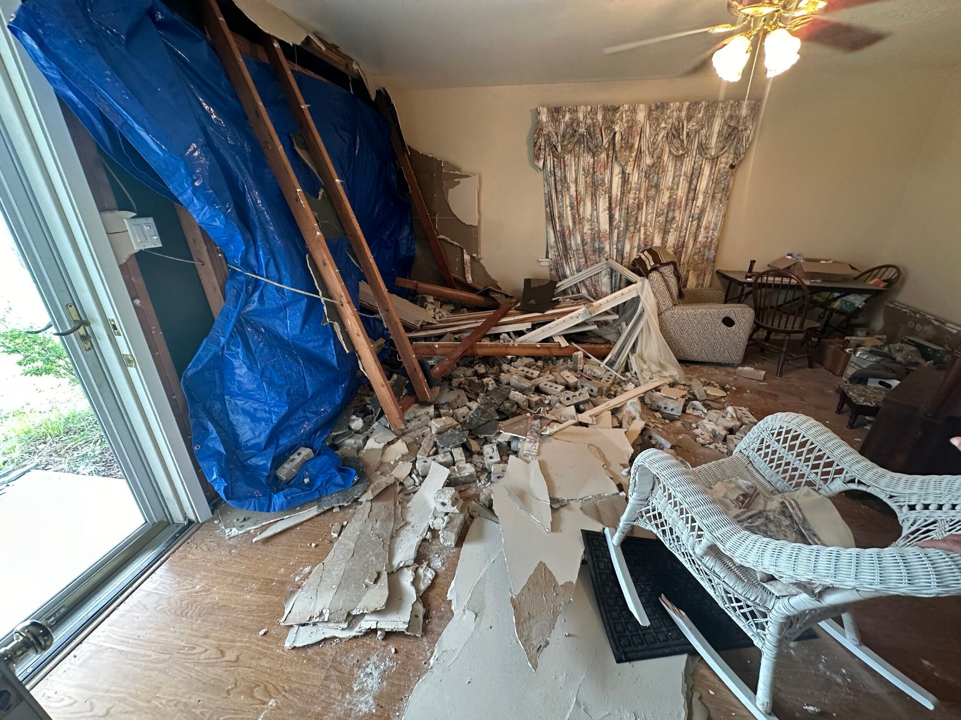 Daytime interior view of the damaged living room in Gretna with brick debris, blown-out framing, and torn drywall after truck impact