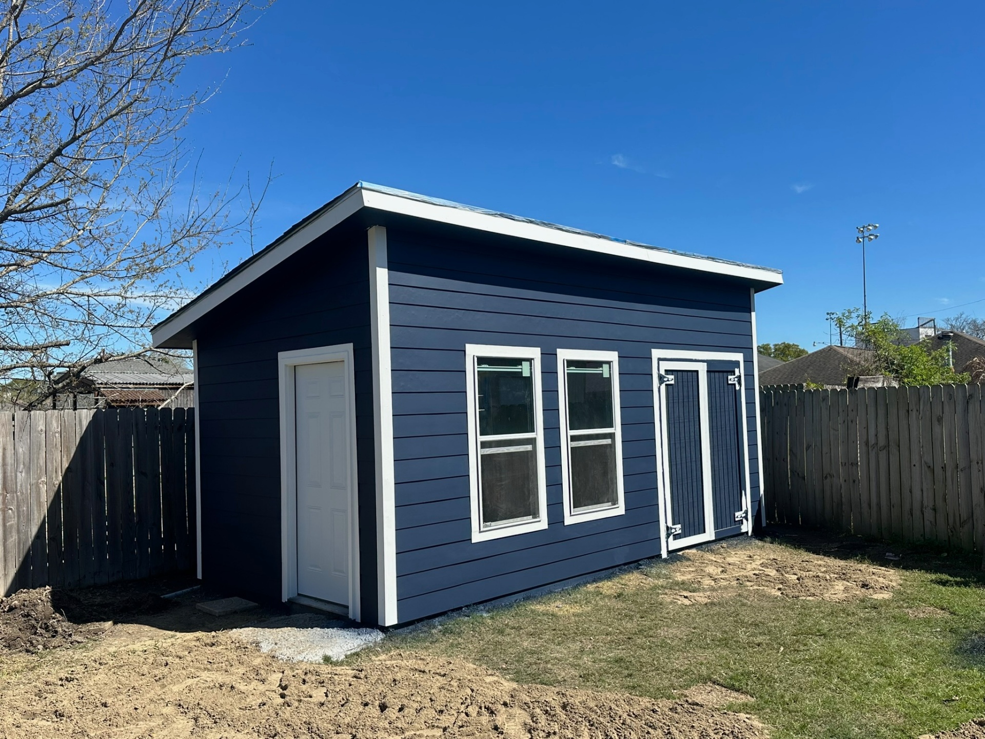 Completed Metairie backyard shed front elevation with navy Hardie siding, white trim, factory side door, double barn doors, and dual windows