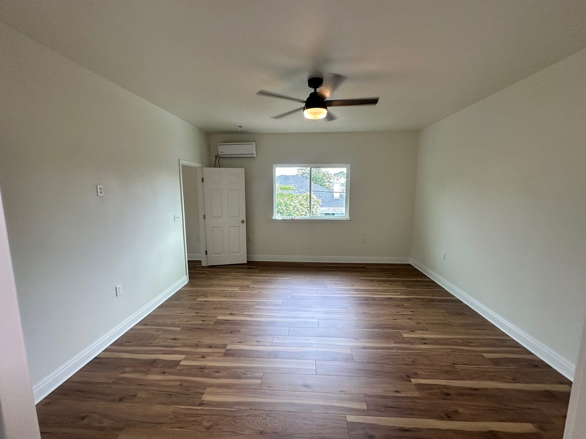 Finished second bedroom on the new second floor of the Metairie addition with wide-plank LVP flooring, white walls and trim, ceiling fan, ductless mini-split and a slider window looking out over neighboring rooftops