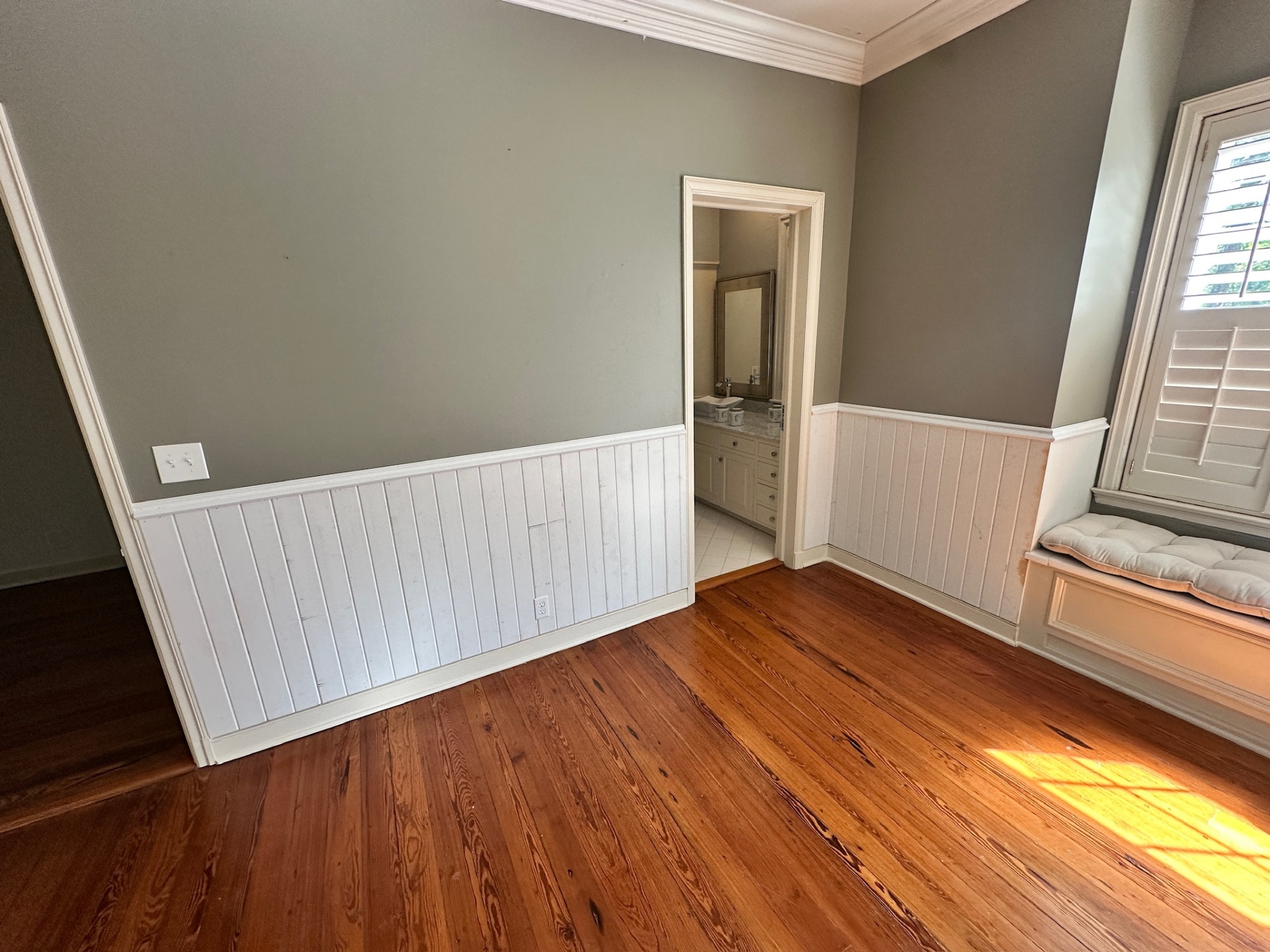 Custom beadboard wainscoting wrapping the doorway into the en-suite bathroom of a Covington Louisiana bedroom with sage green walls and window seat