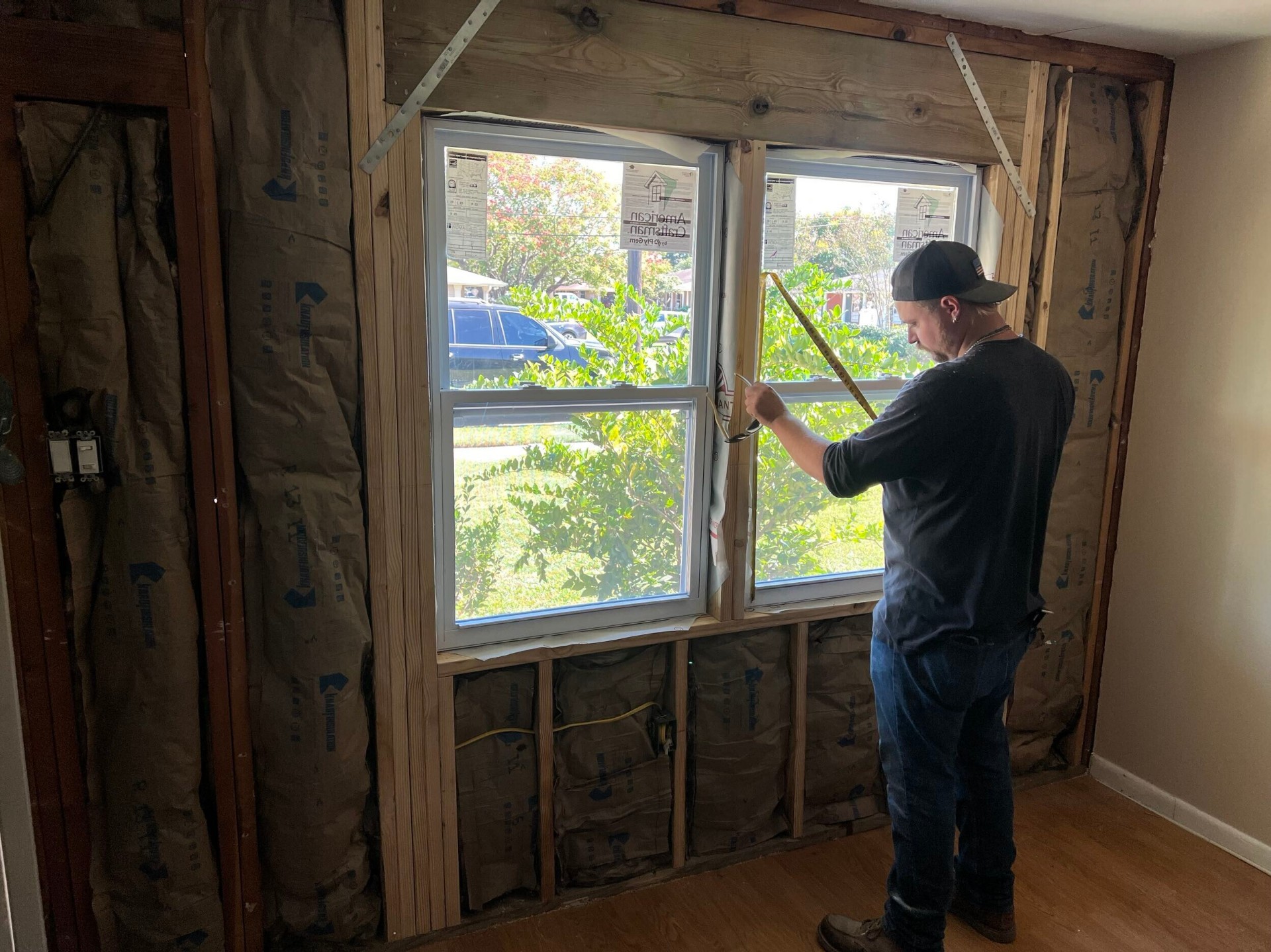 Cajun Home Services crew member measuring the new window opening from inside the Gretna home with fresh batt insulation installed in the wall cavities