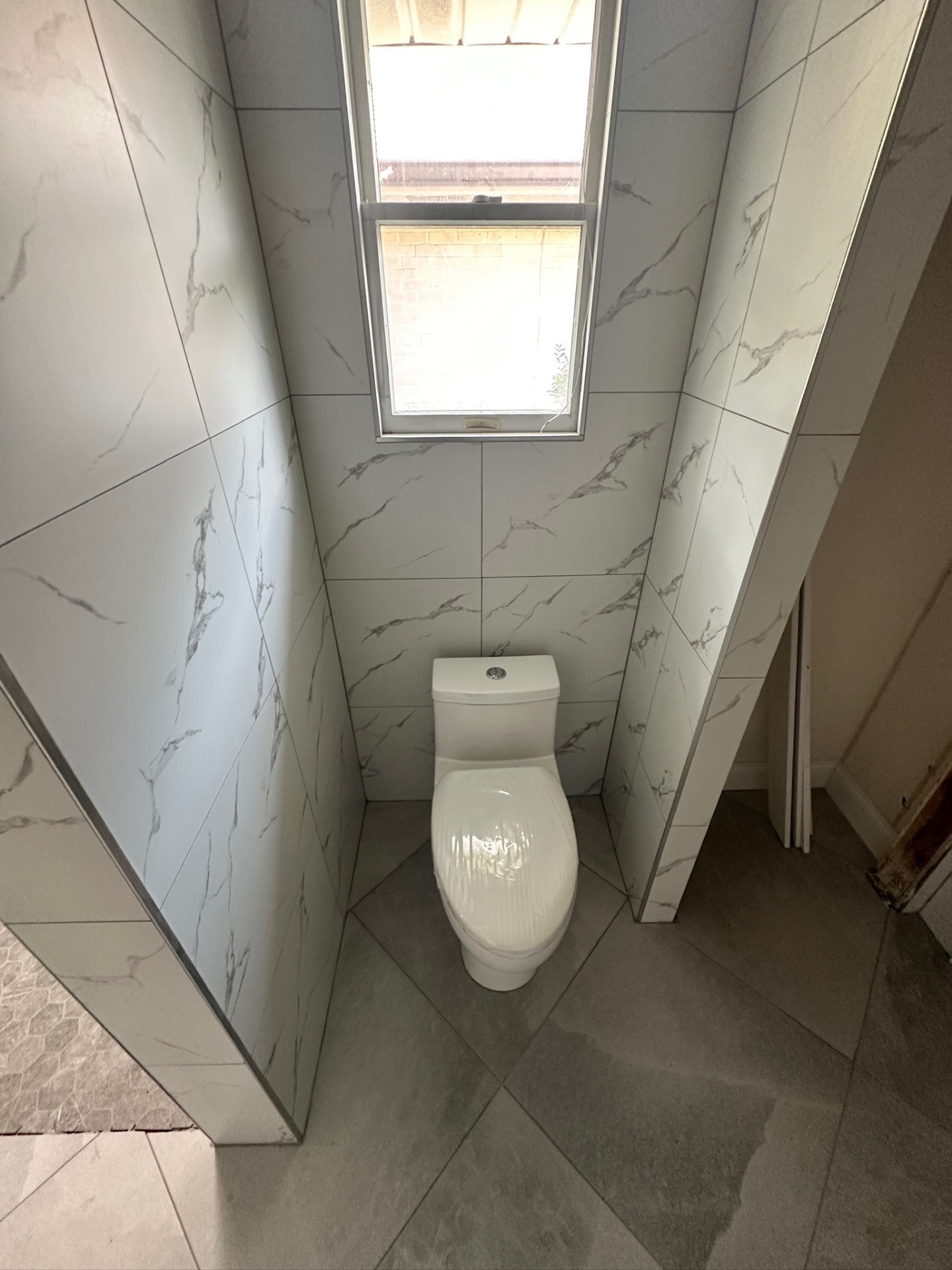 Finished tiled water closet with marble-look walls and one-piece toilet in Metairie master bath