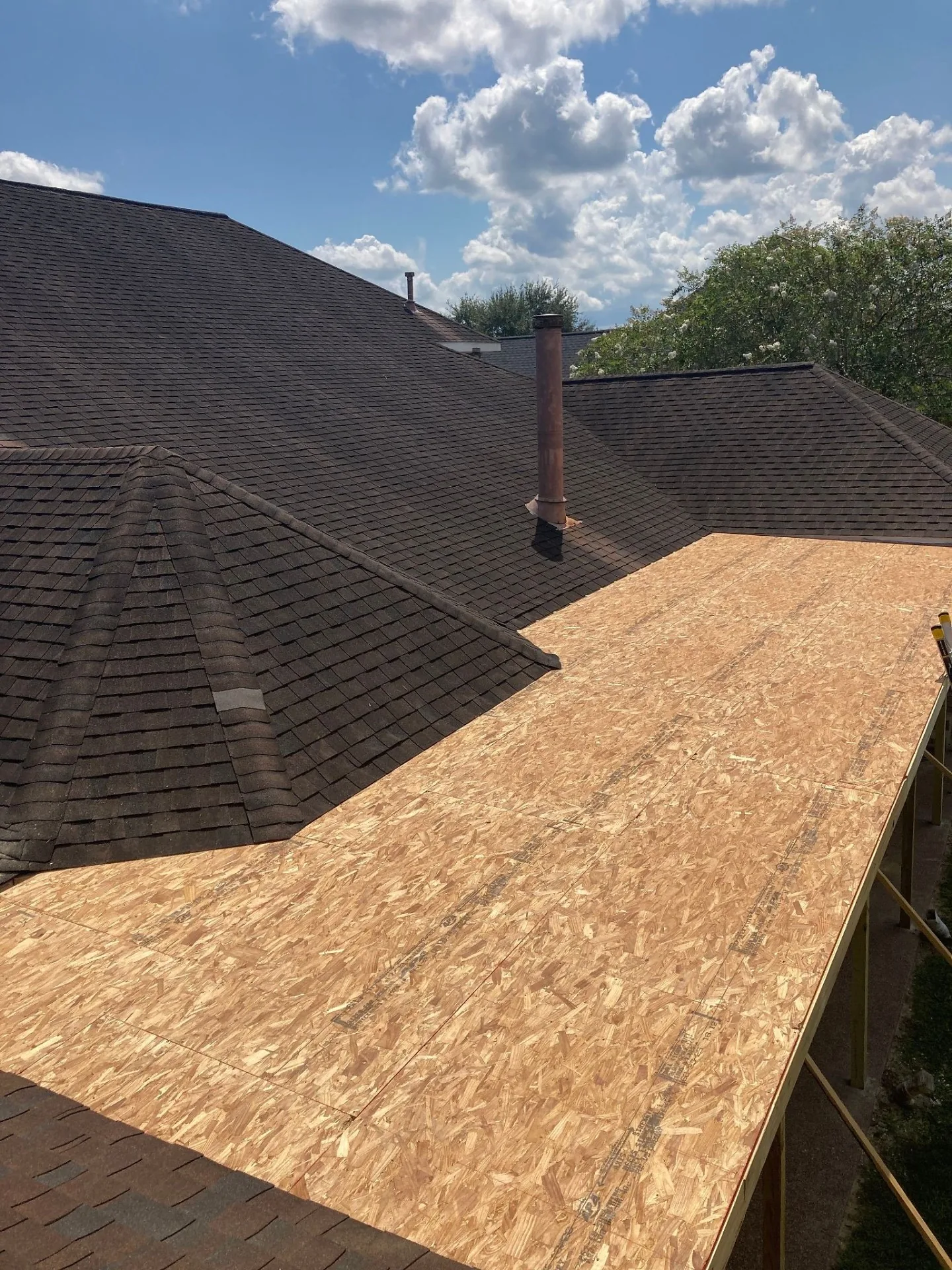 Aerial view of new OSB roof decking installed on covered patio tied cleanly against main shingle roof of Destrehan Louisiana home before shingle install