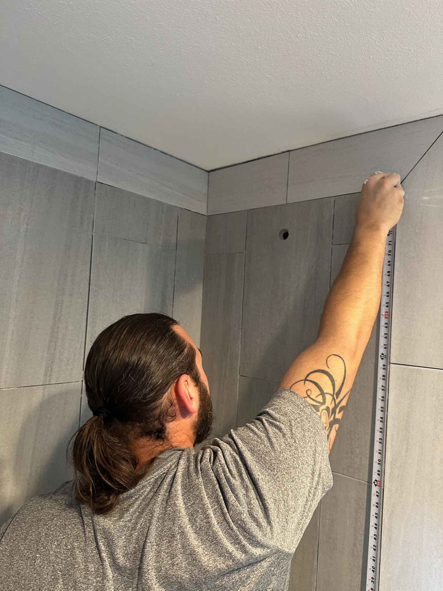 Installer measuring the top course inside the master bath shower of the Metairie second-floor addition to keep the tile layout even tight to the ceiling line
