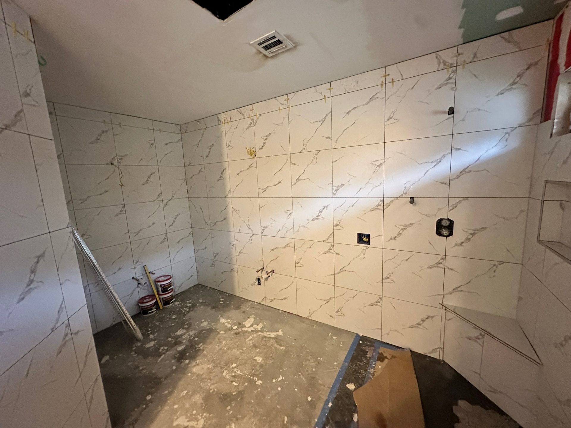 Shower back wall fully tiled in marble-look porcelain with valve and shower head stubs and vent framed in Metairie master bath
