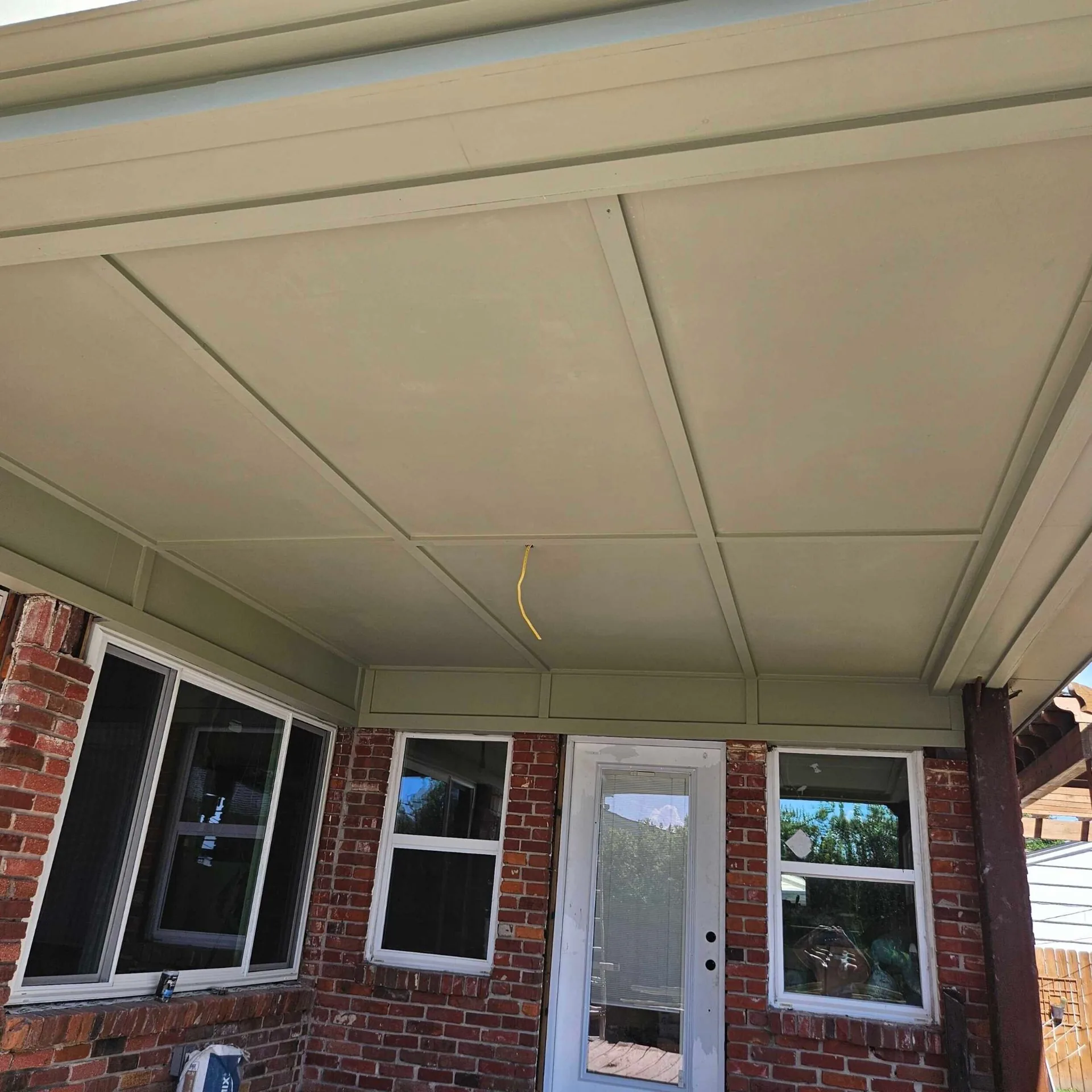 Finished covered porch ceiling at Blanke Street Metairie home with painted vinyl beadboard, green trim, and preserved brick columns over the original brick wall