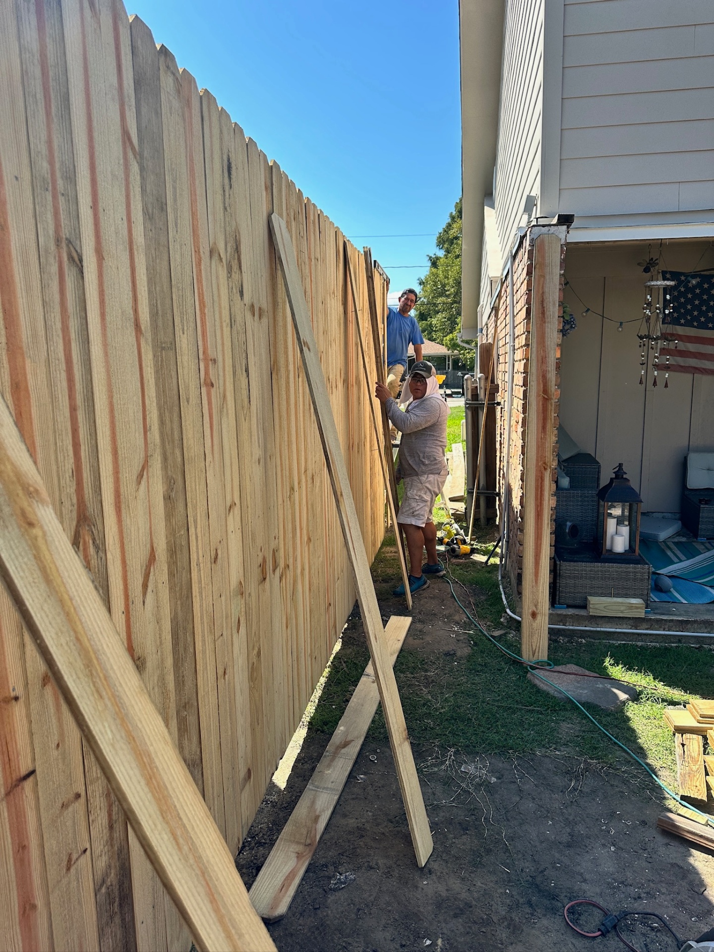 Two Cajun Home Services carpenters installing dog-eared pressure-treated pickets in the tight side yard between the new second-floor addition and the neighboring house