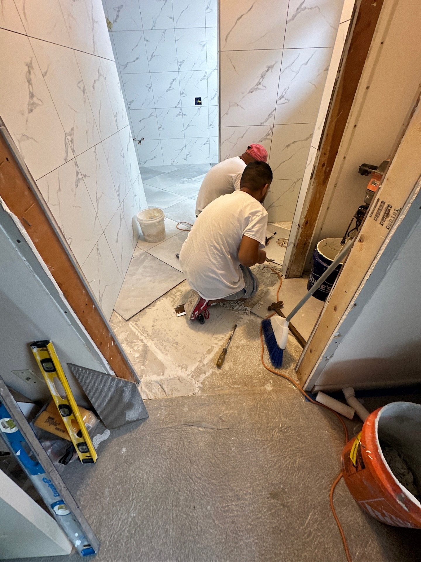 Tile crew working the threshold and toilet room entry with marble-look porcelain in Metairie master bath