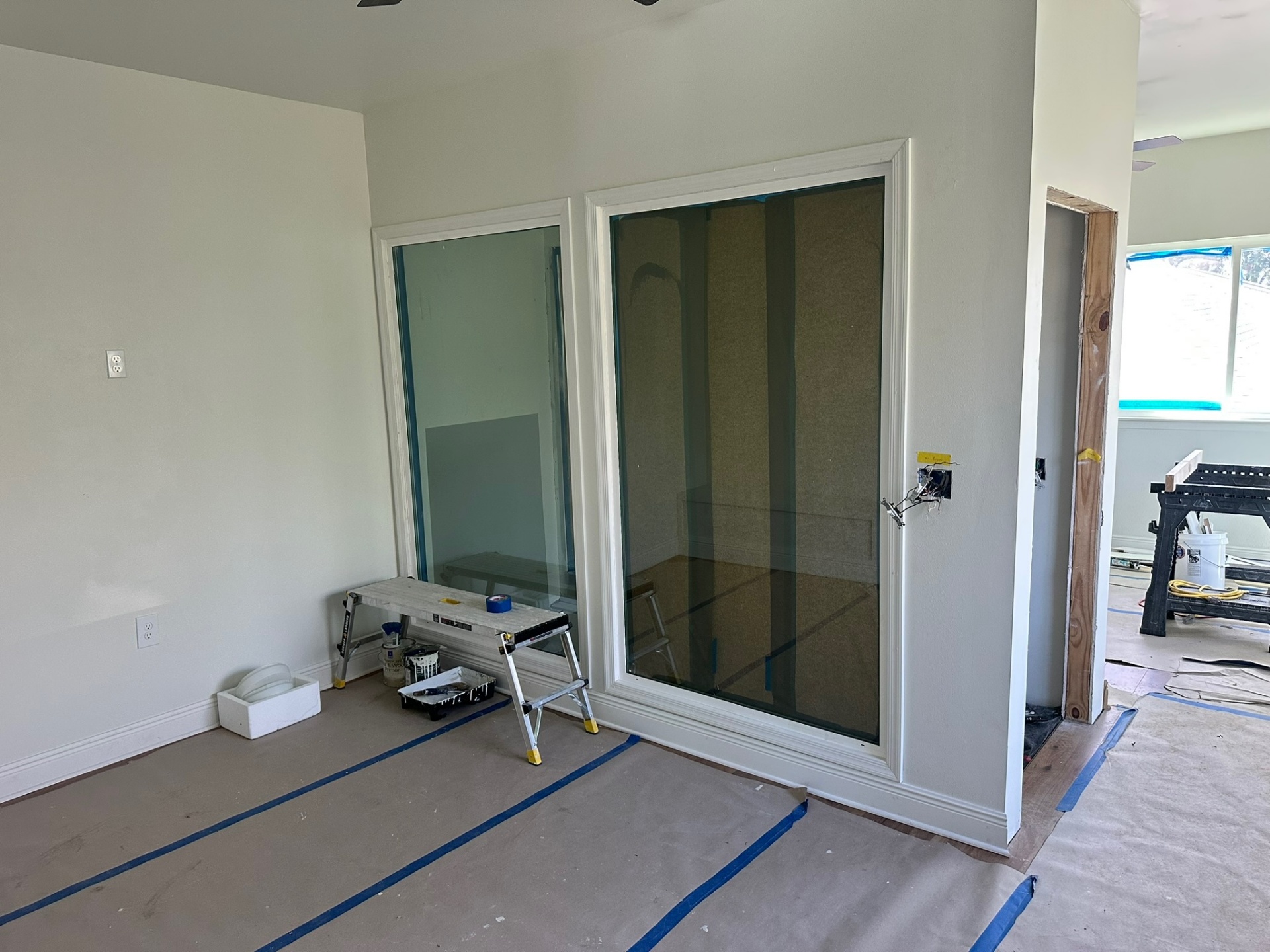 Newly installed interior sliding glass door with white casing in second-floor addition, drop cloth and ladder staged for paint prep