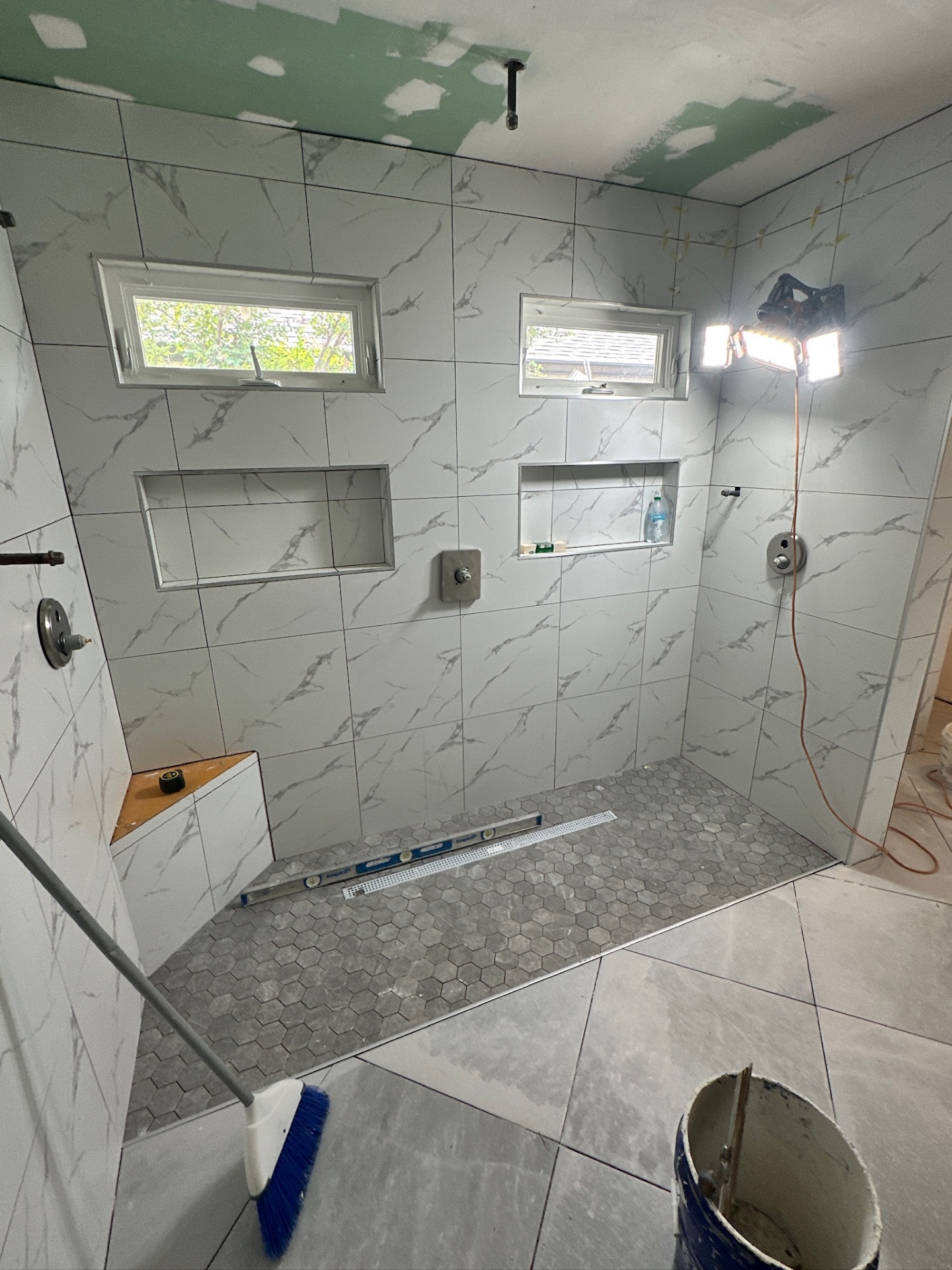 Wide walk-in shower with dual shower heads, dual niches, dual awning windows, and hex mosaic floor in Metairie master bath