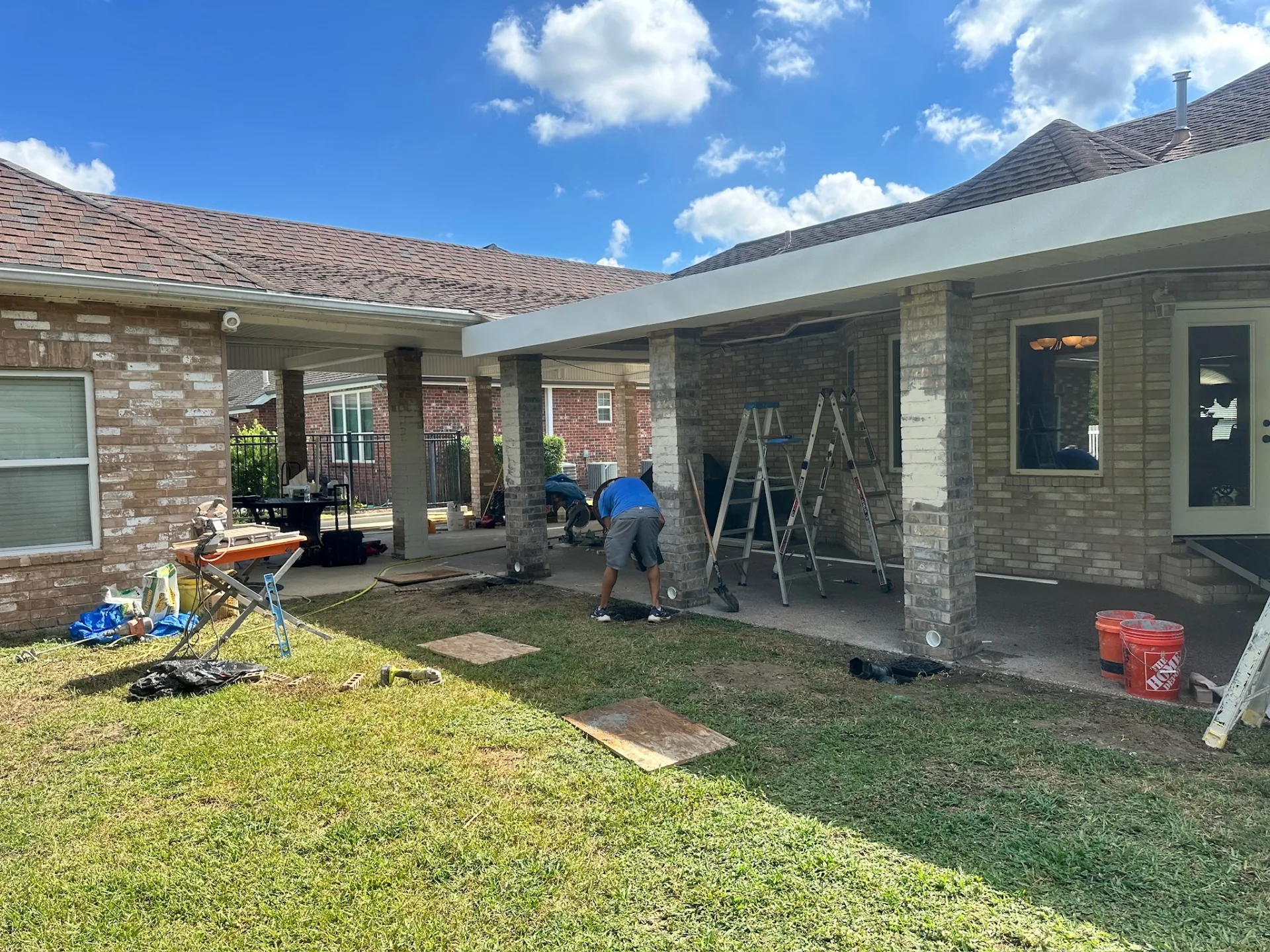 Wide yard view of rebuilt covered patio with limewashed brick posts and soffit installation underway at Destrehan Louisiana home