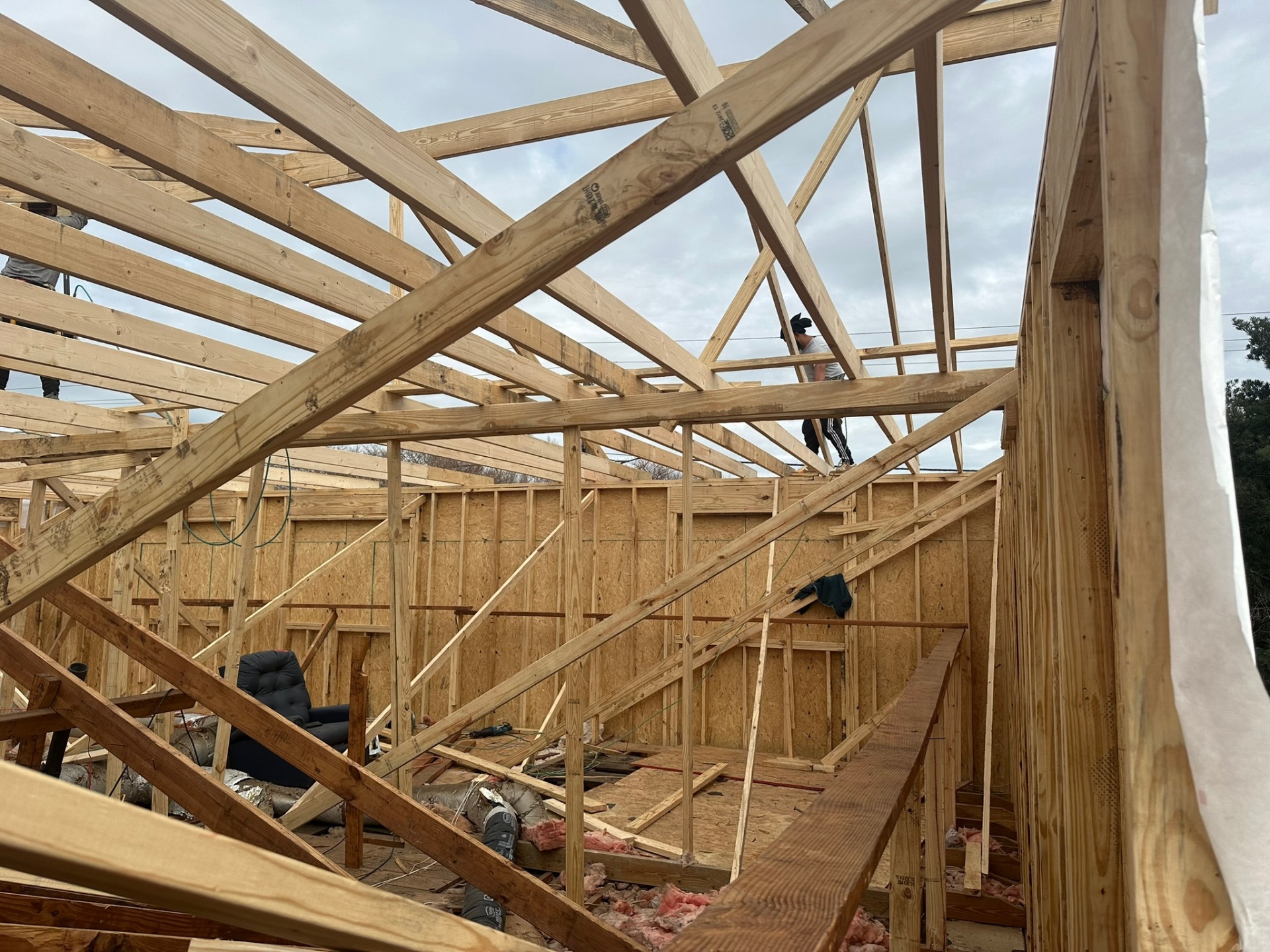 Interior view from inside Metairie second-floor framing with new roof rafters overhead and a carpenter walking the top plates while setting more members