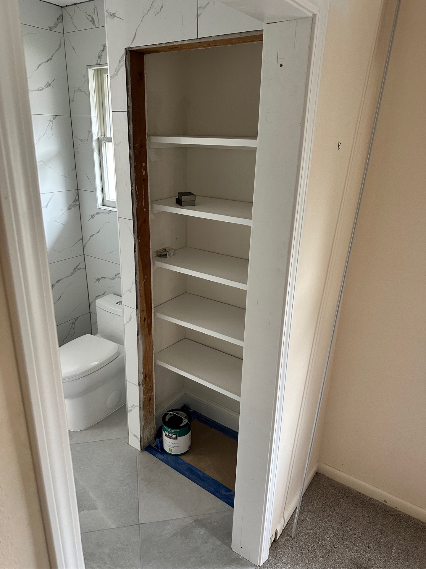 Built-in linen closet with fresh white paint and tile-wrapped opening next to the water closet in Metairie master bath