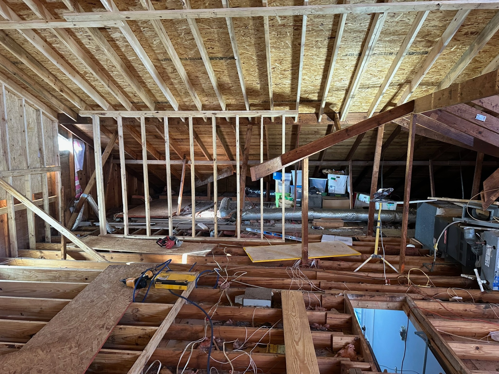 Wide interior view inside Metairie attic with new knee wall framing standing under existing roof rafters, original HVAC equipment and ductwork visible behind the new wall line