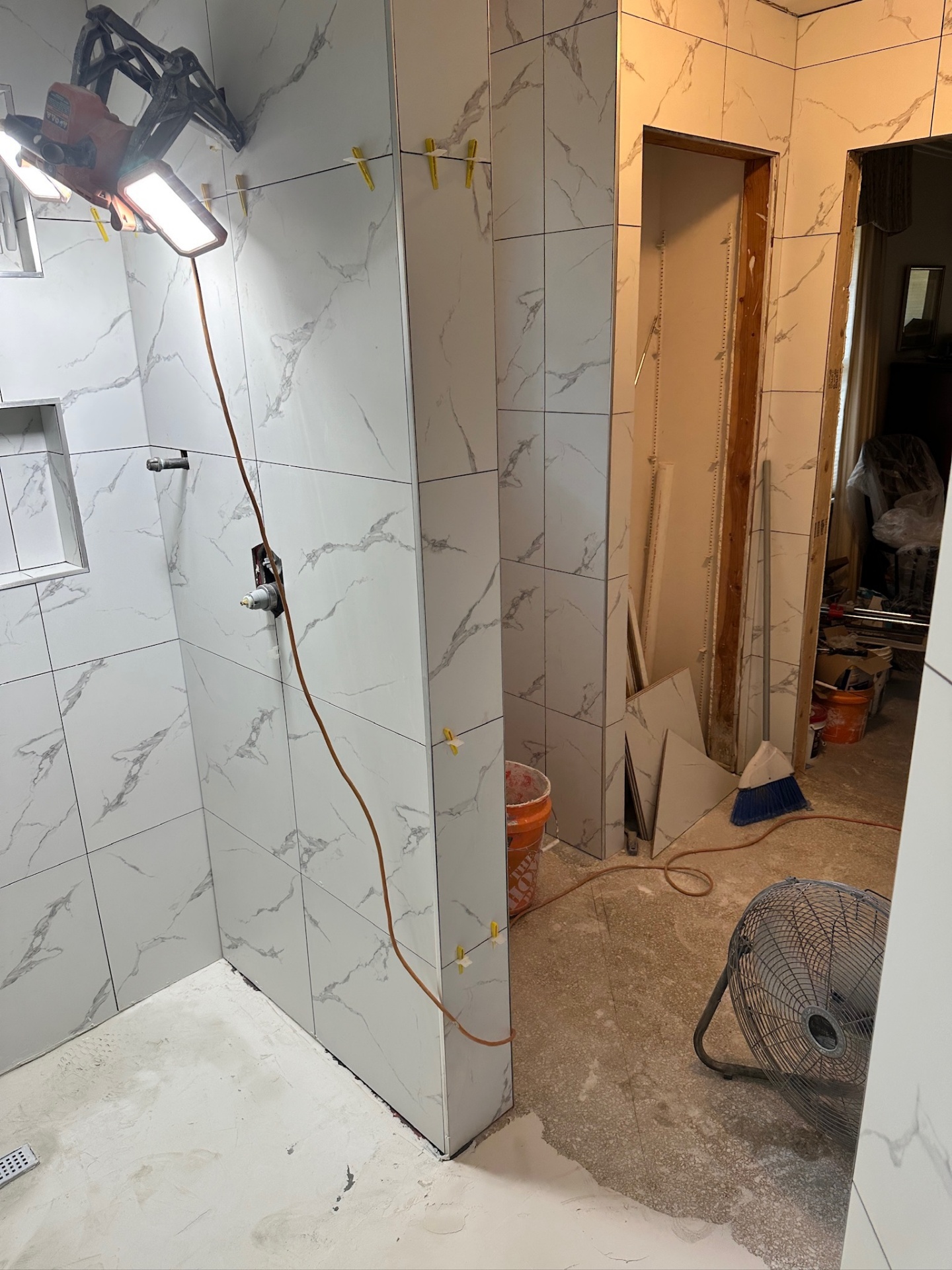Shower wall corner mid-tile with valve stub and Schluter edges, work lights and fan running in Metairie master bath