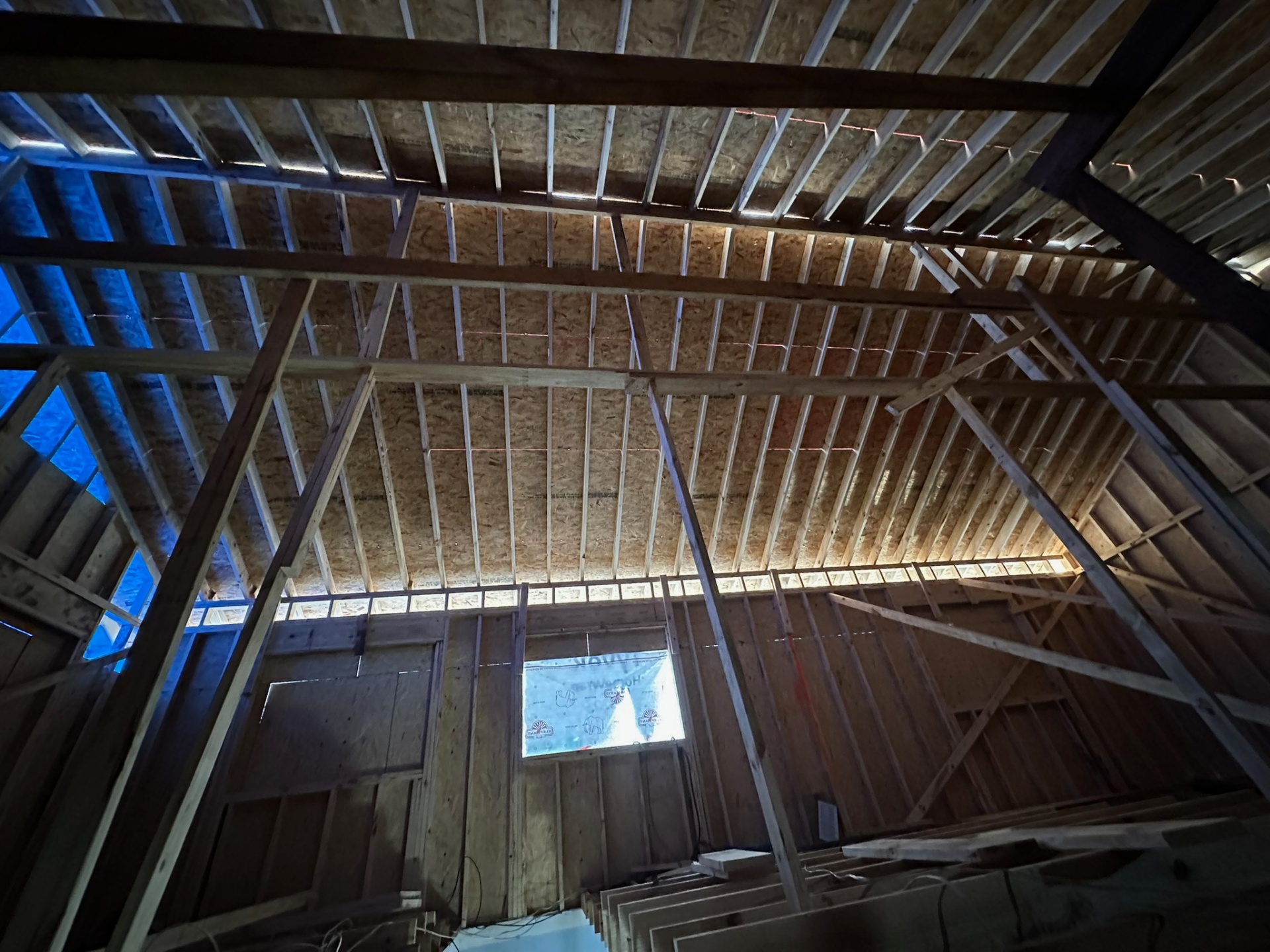 Interior view of new roof rafters and OSB decking installed on Metairie second-floor addition with Tyvek window covering on gable end