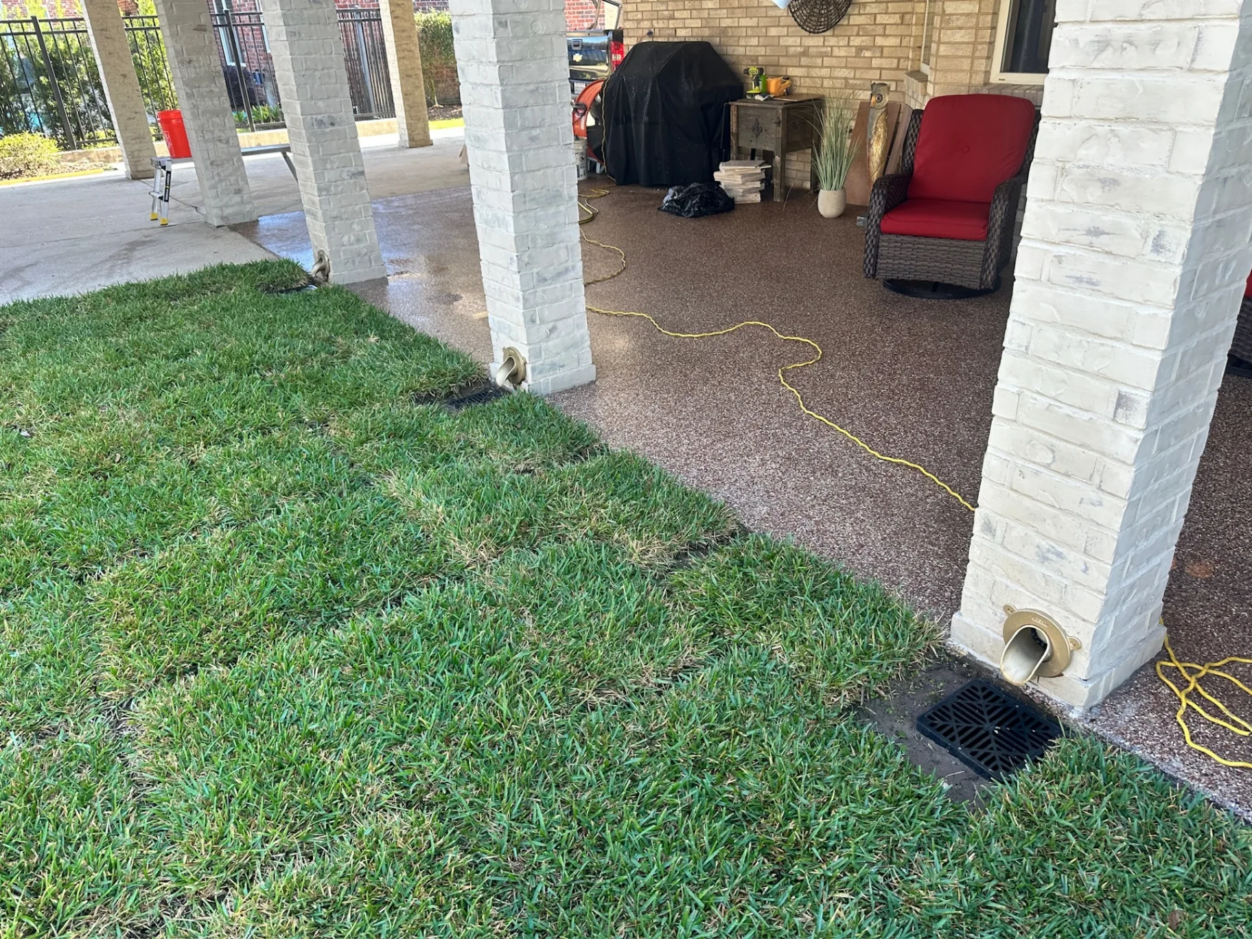Wide finished view of rebuilt covered patio at Destrehan Louisiana home with limewashed brick posts, epoxy pebble deck, and hidden downspout drain grates at each post base