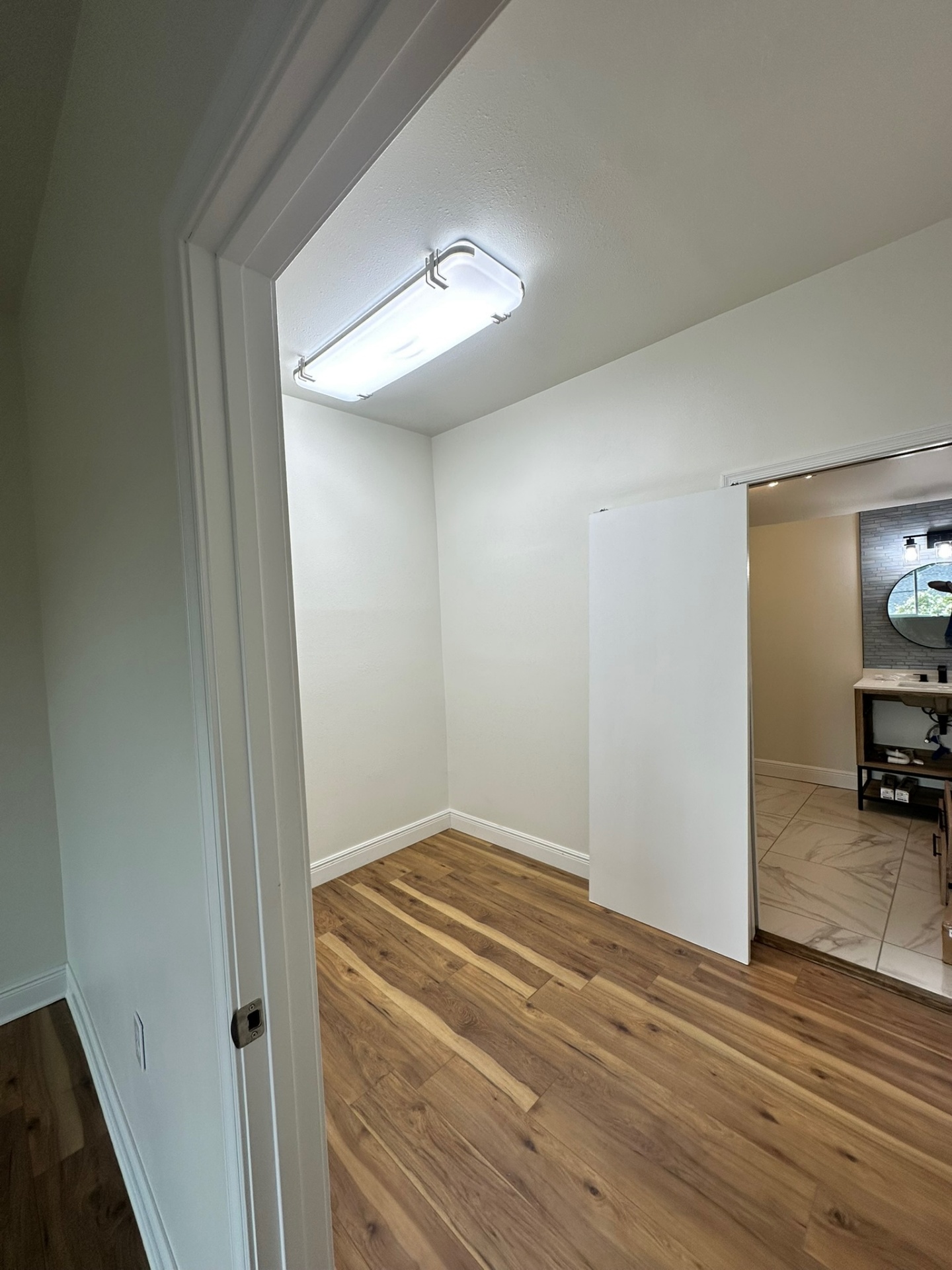 Finished walk-in closet on the new second floor of the Metairie addition with LED ceiling fixture, wide-plank LVP flooring and clear sightline through the doorway into the master bathroom with marble tile floor and floating wood vanity