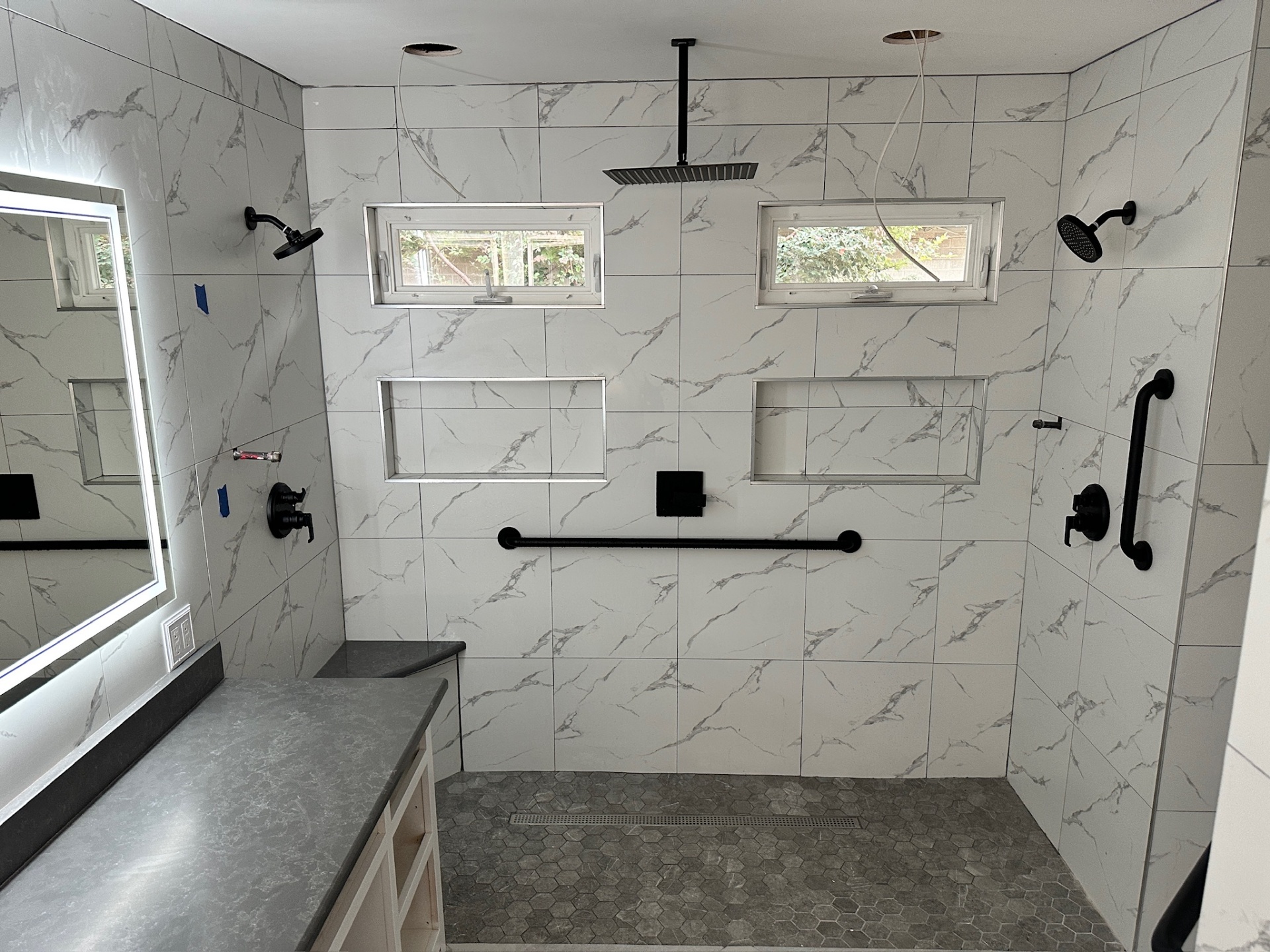 Walk-in shower with dual shower heads, ceiling rain head, black grab bars, dual niches, and hex mosaic floor in Metairie master bath